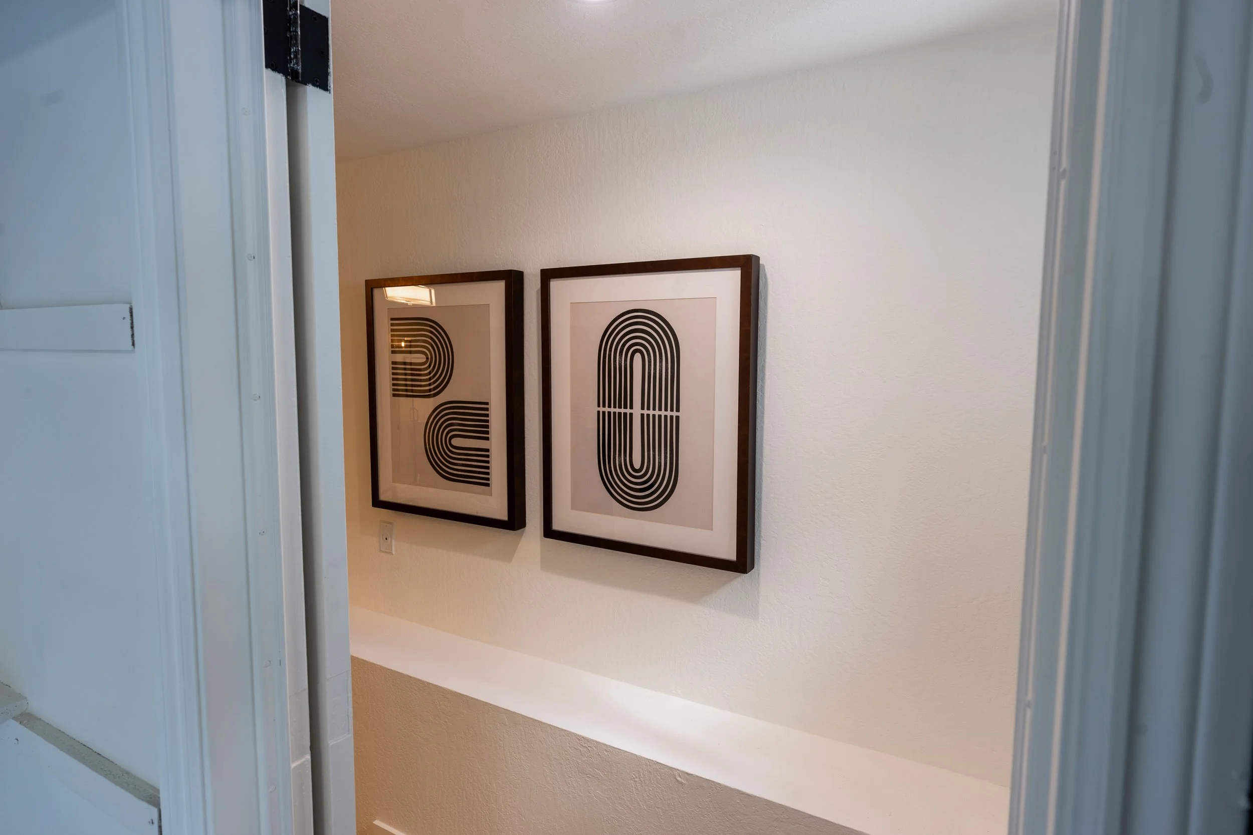 Two framed abstract black and white prints hanging on a white wall in a hallway.