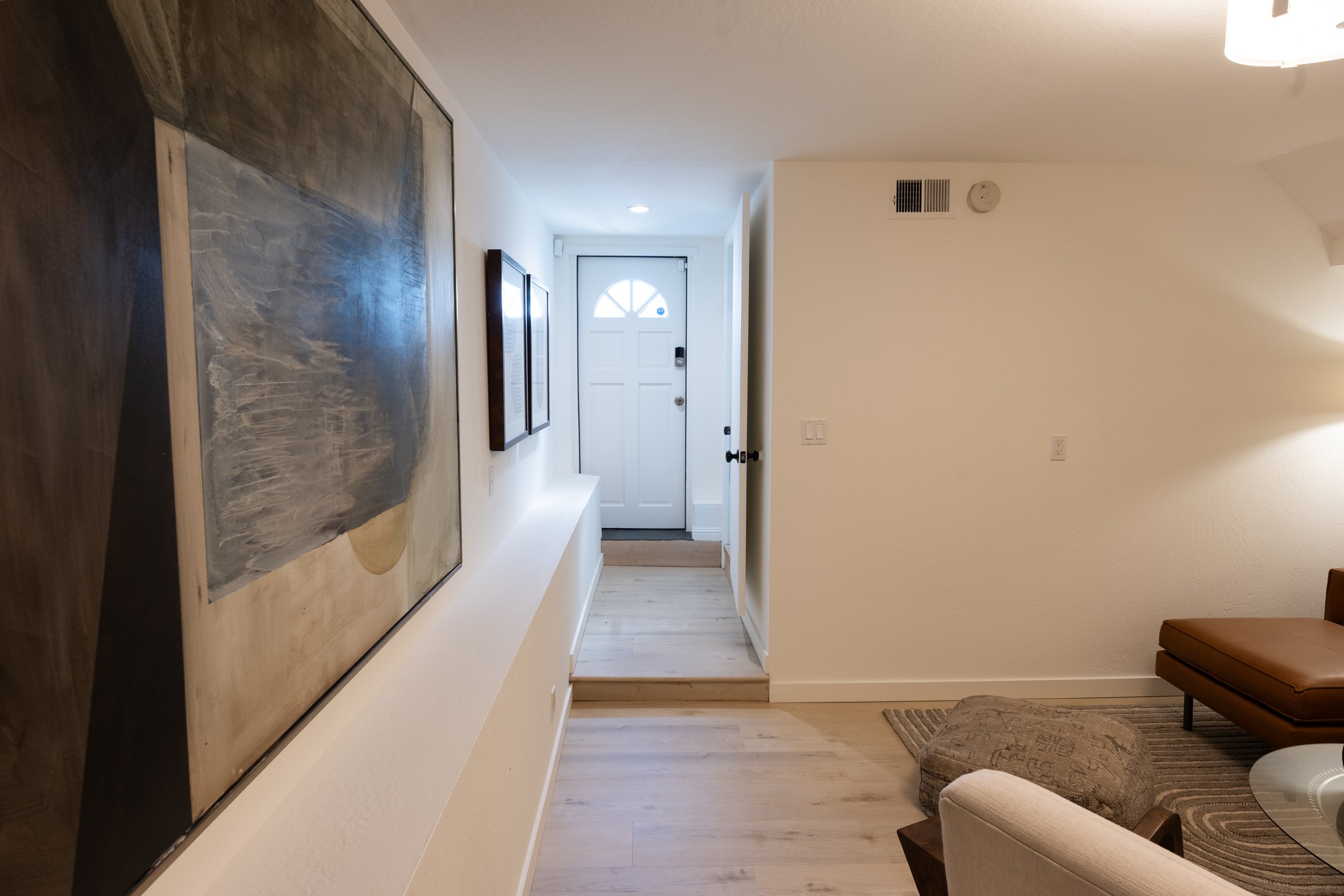 Entryway with white door, framed artwork on wall, and seating area with rug and chair.