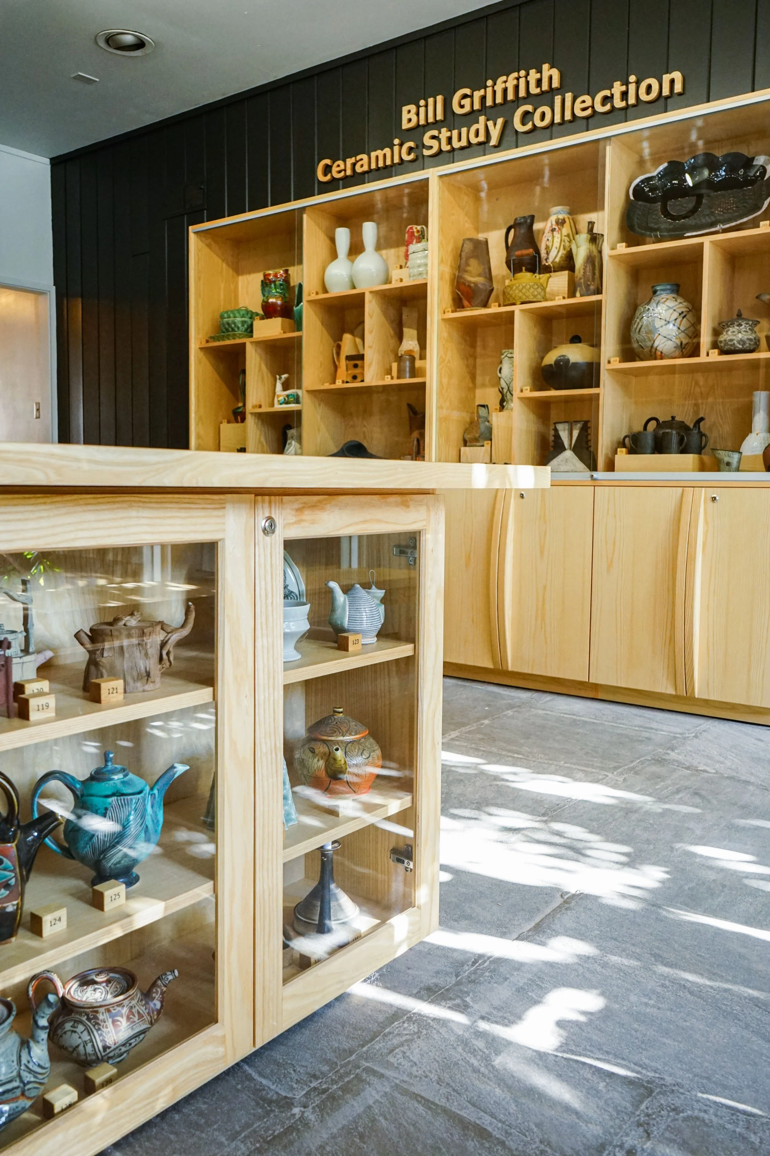 Wooden display case filled with colorful ceramic vases, cups, and decorative items inside a ceramics study collection room.