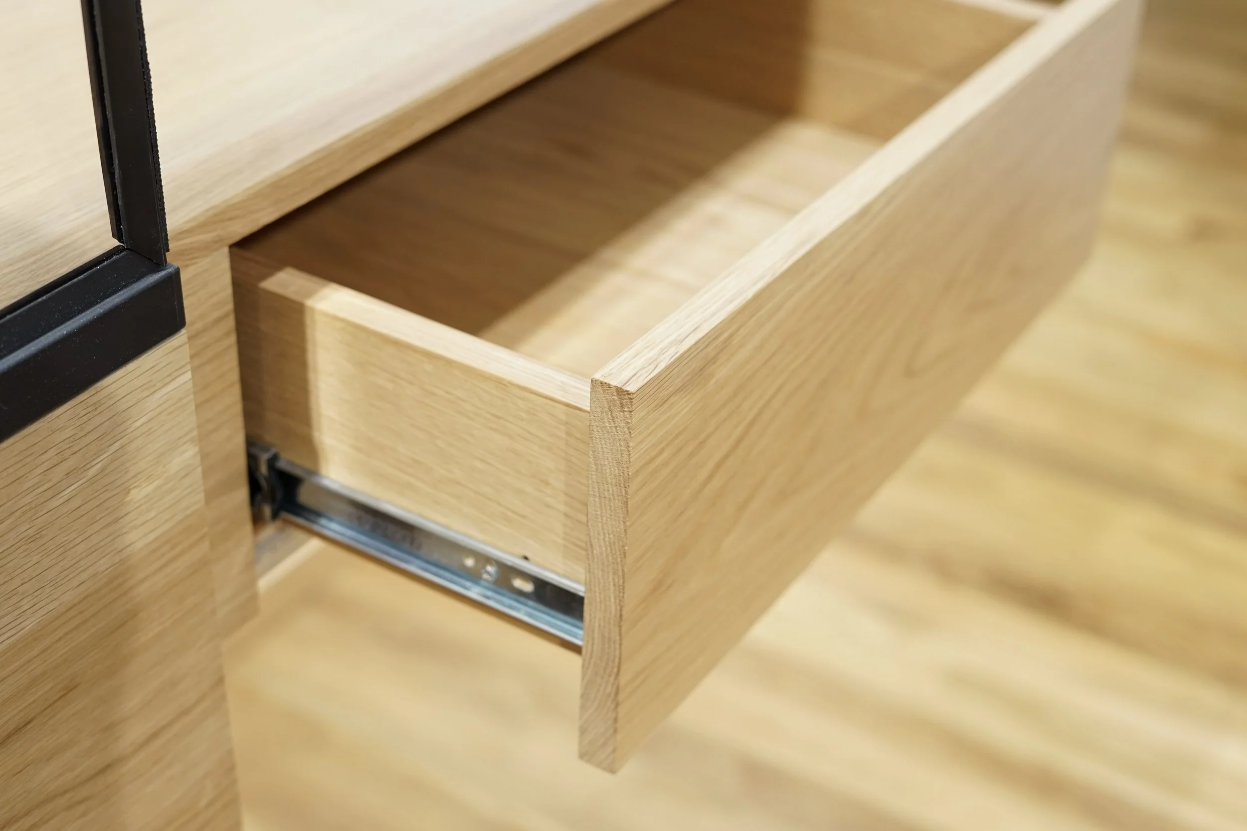 A close-up image of an open wooden drawer with no contents, showing the wood grain and the metal sliding mechanism.