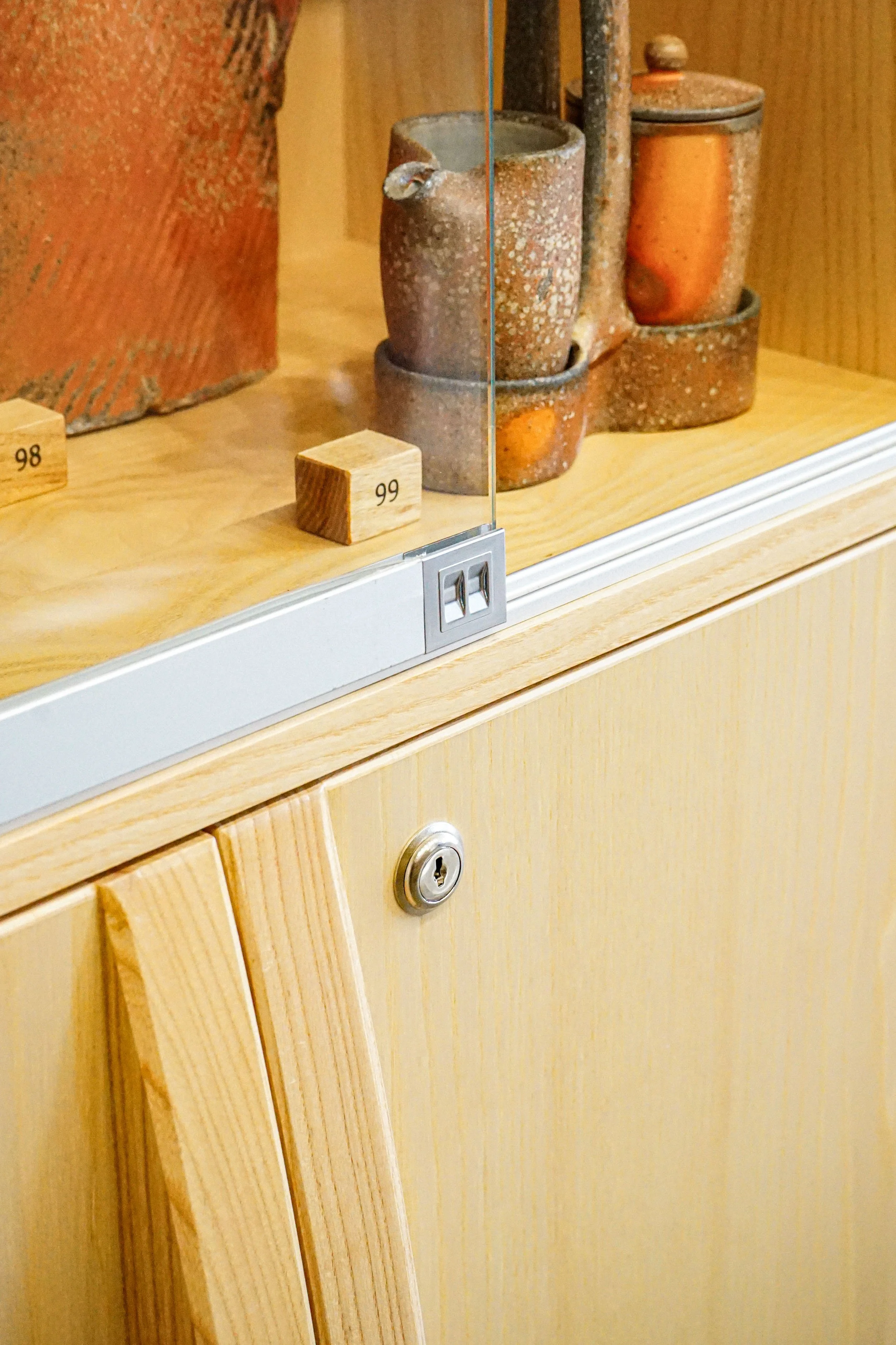 Detail of wooden display case with three ceramic cups and lids on a light wooden shelf.