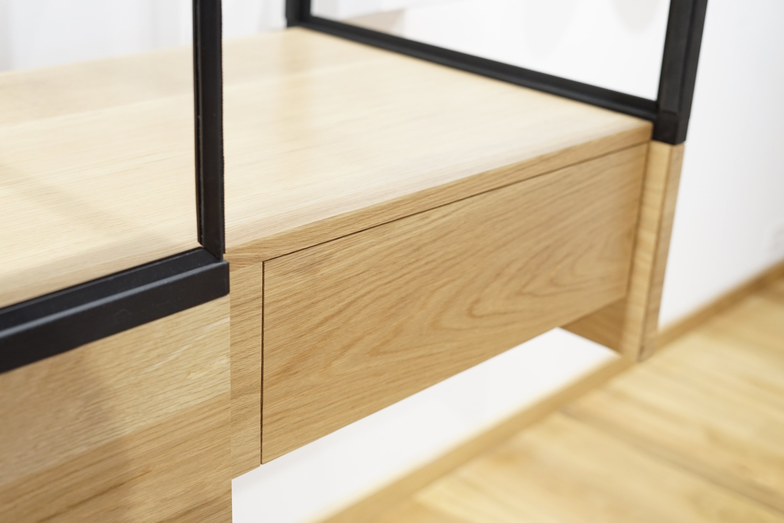 Close-up of a modern wooden and black metal furniture piece, possibly a shelf or cabinet, with a light wood finish and minimalist design.
