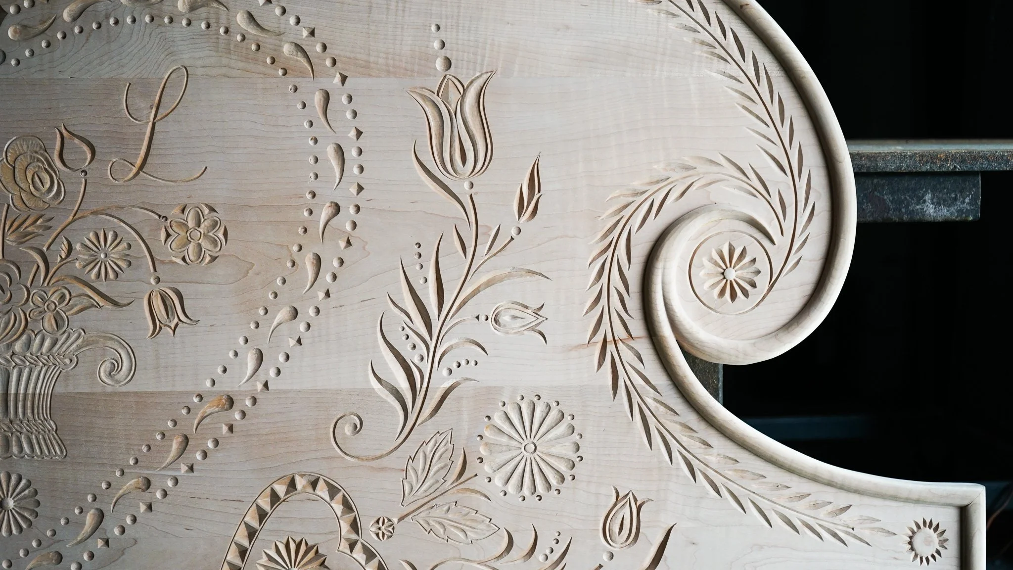 Carved wooden surface with floral and decorative patterns, including tulips, daisies, and leaves.