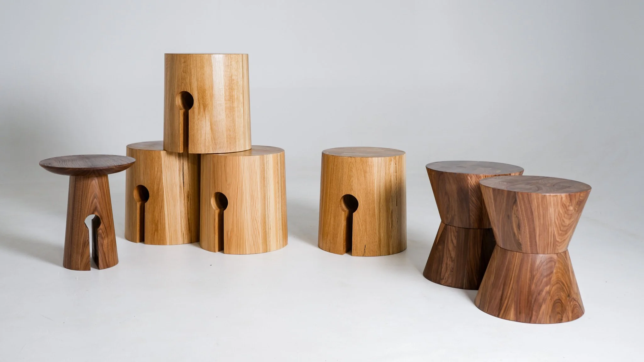A collection of wooden side tables of varying heights and shapes arranged on a white surface against a plain white background.