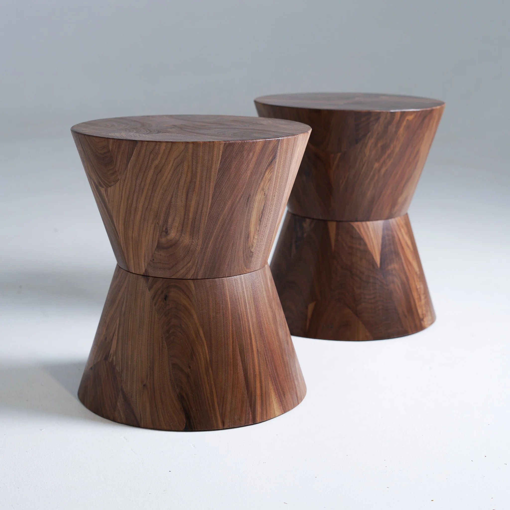 Two walnut wooden side tables with a smooth, polished surface and conical shape, placed on a plain white background.