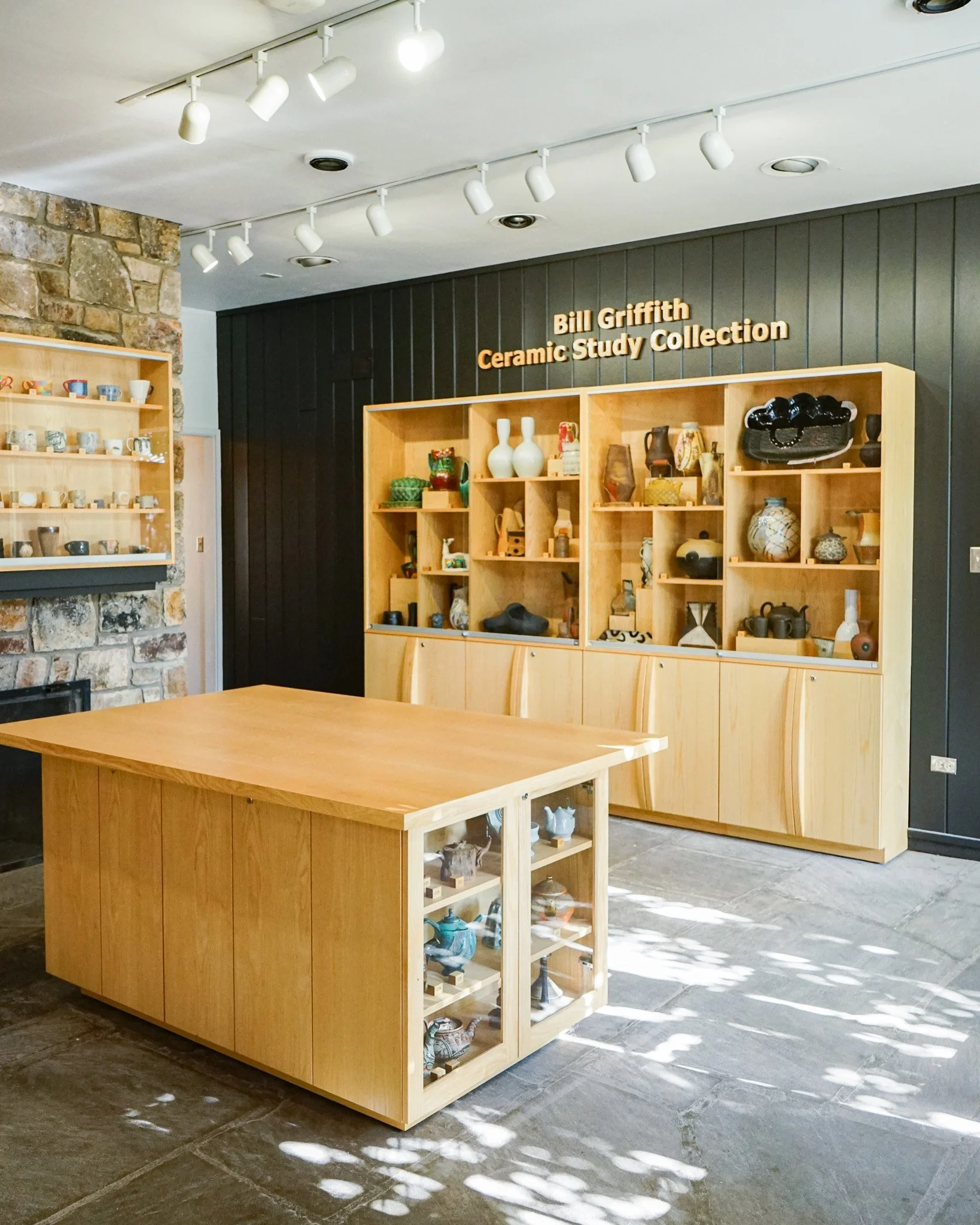 A display of ceramic pottery pieces on wooden shelves in a gallery space, with a sign indicating it is part of the Bill Griffith Ceramic Study Collection.
