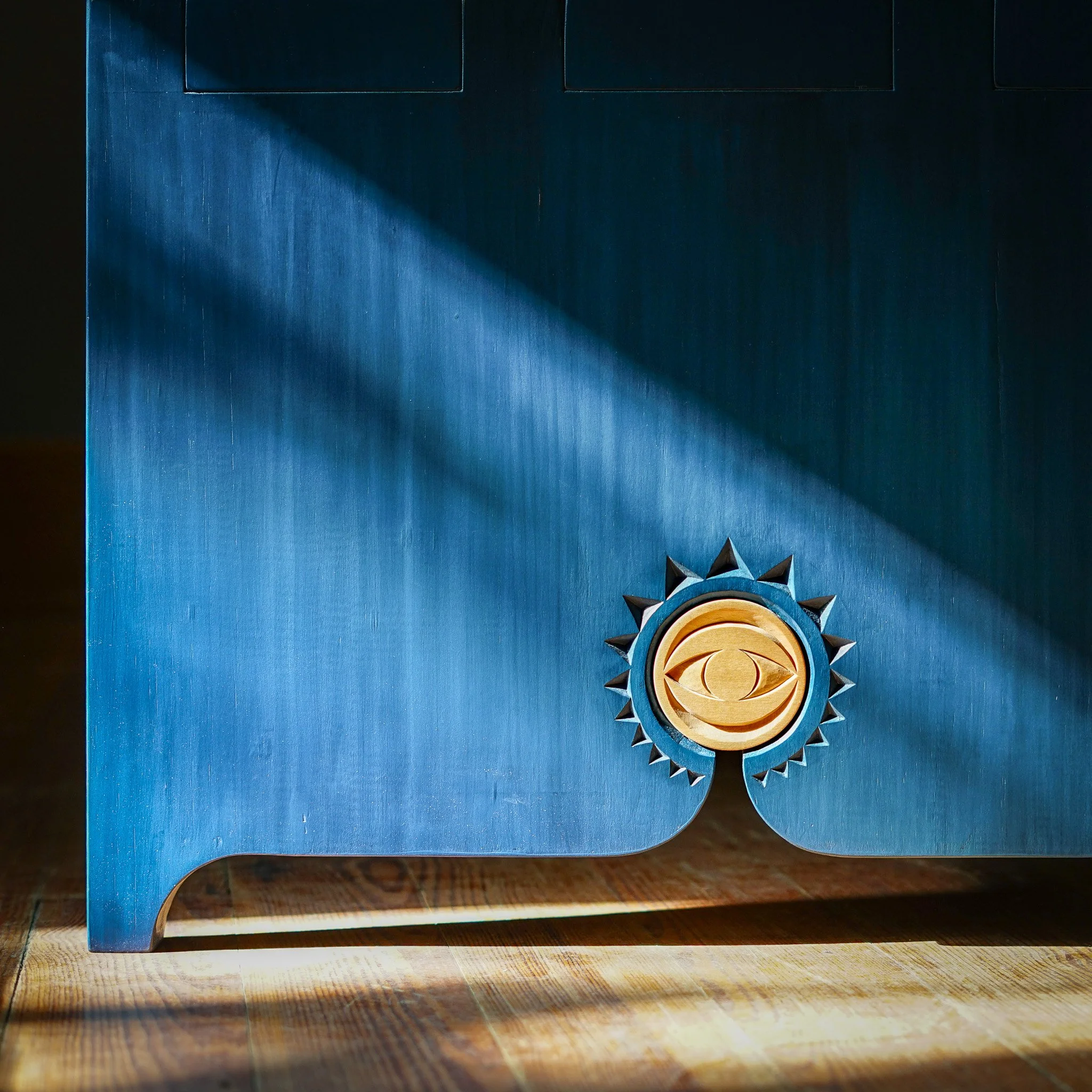 A blue wooden coffee table with a decorative hand carved wooden medal, partially illuminated by a light source from the left side of the image.