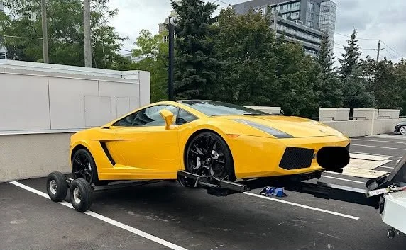 Yellow sports car on a trailer in a parking lot.