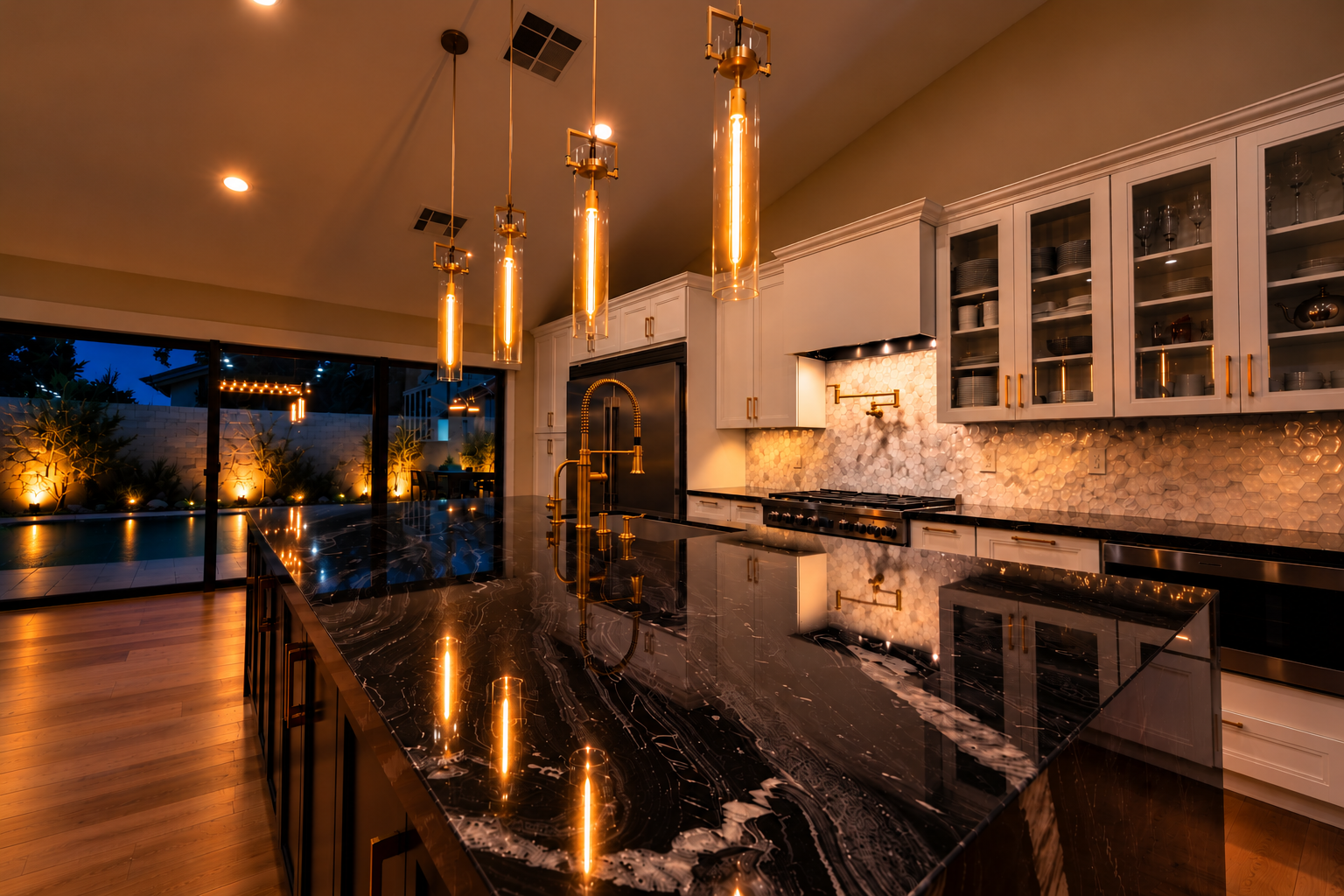 Modern kitchen with black and gold accents, featuring a large black marble island, gold pendant lighting, open glass-front cabinets, and a view of a backyard with a pool and outdoor seating.