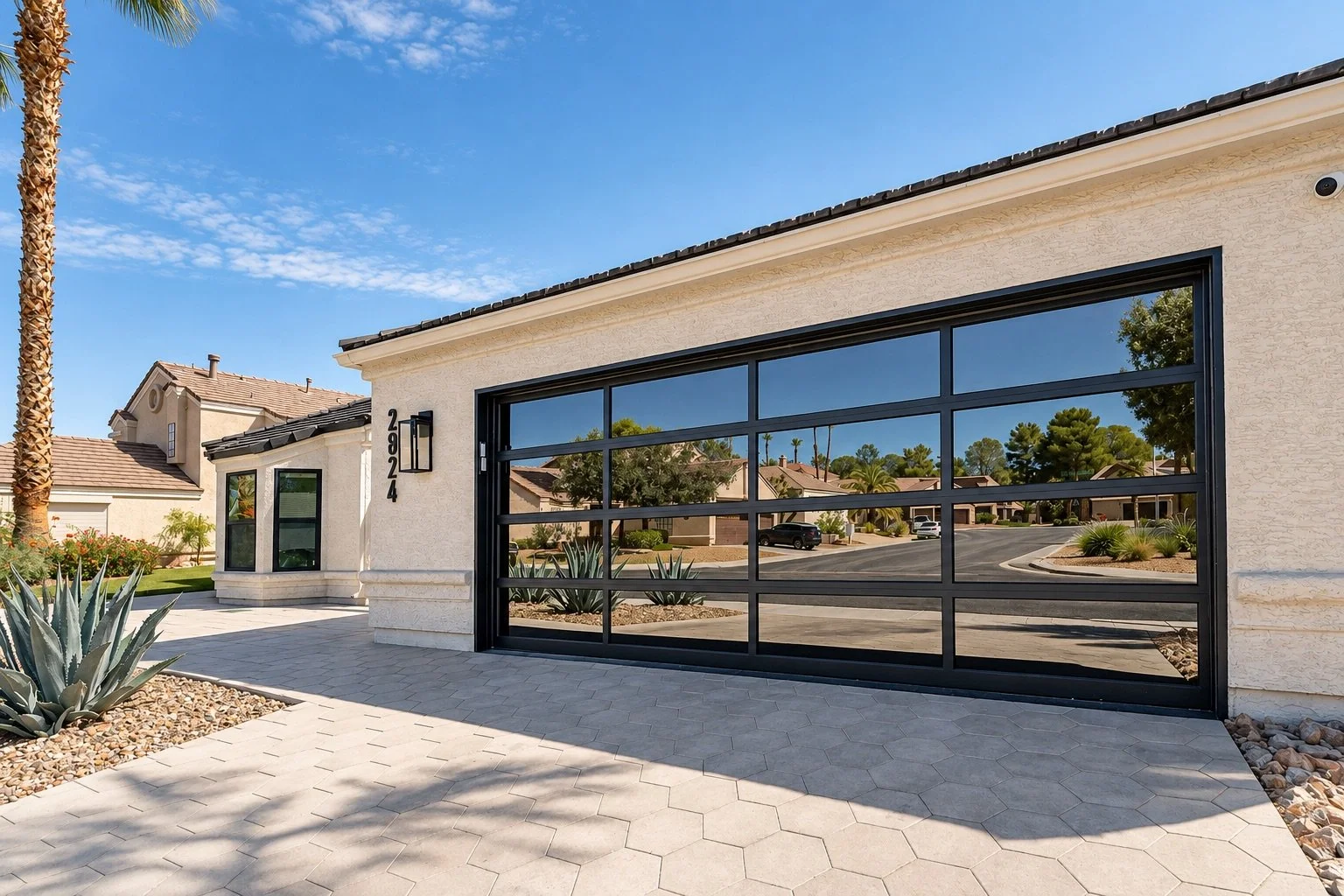 A modern house with a large black-framed glass garage door, desert landscaping, and a clear blue sky.