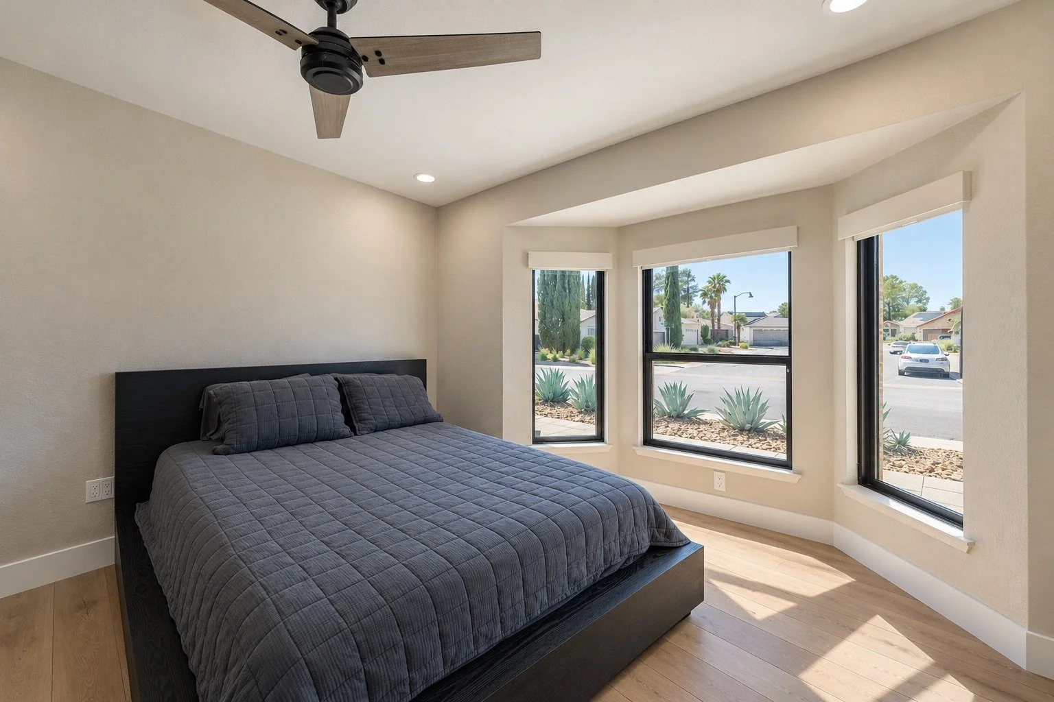 Bedroom with a large bed, dark furniture, and large windows showing a view of a neighborhood with trees and parked cars.