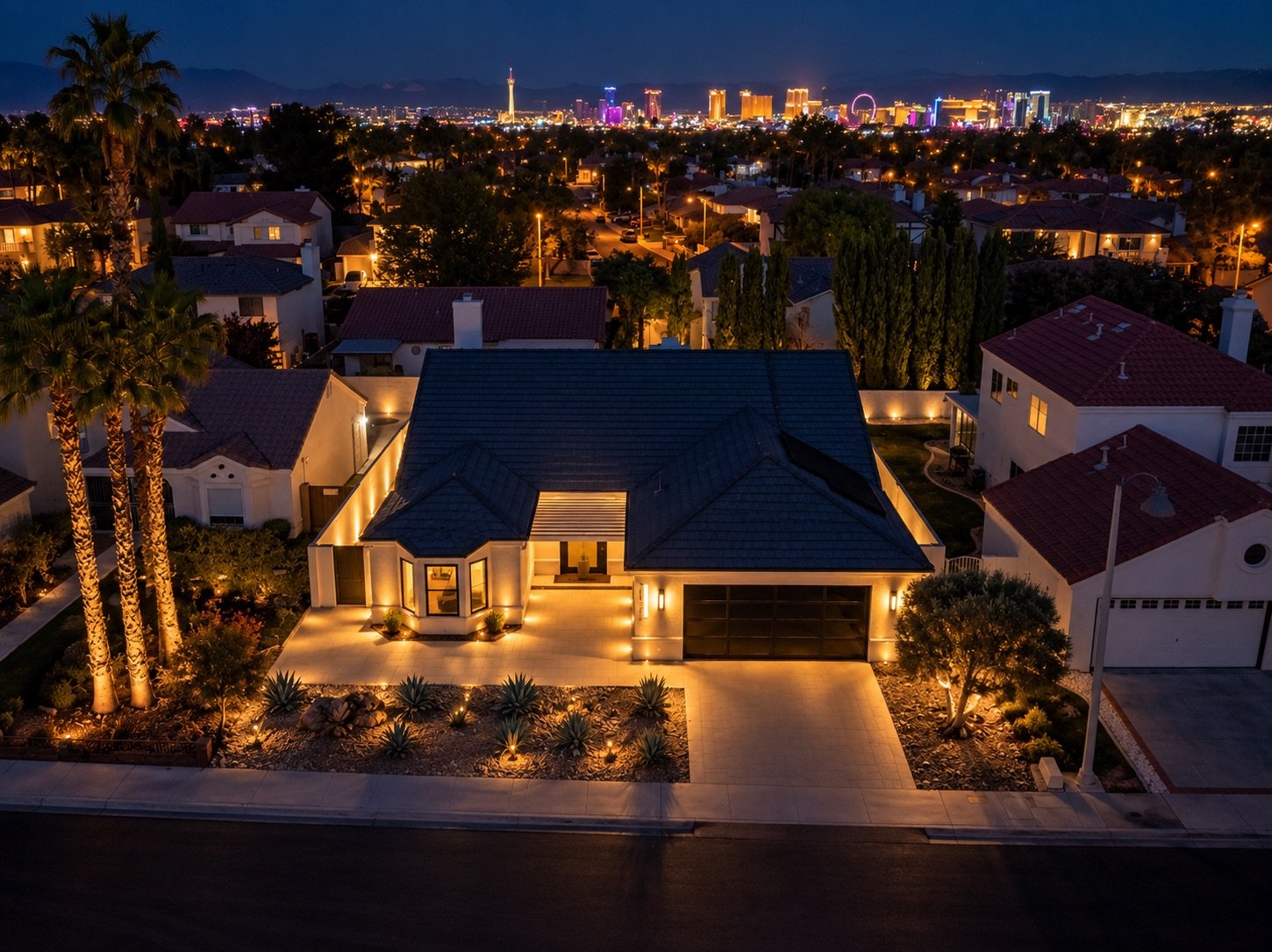 A lit modern house in a suburban neighborhood at night, with a city skyline and illuminated buildings in the distance.