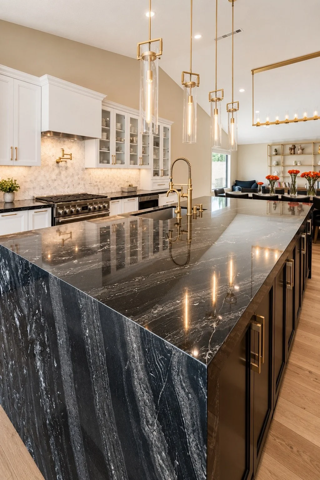 Modern kitchen with black marble countertop and gold fixtures, open to dining and living area with flowers and shelves.