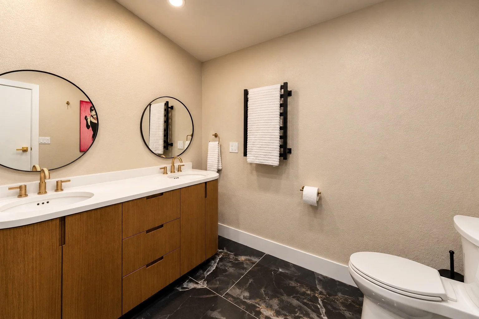 Modern bathroom with double sink vanity, round mirrors, white towels, a toilet, and black marble flooring.