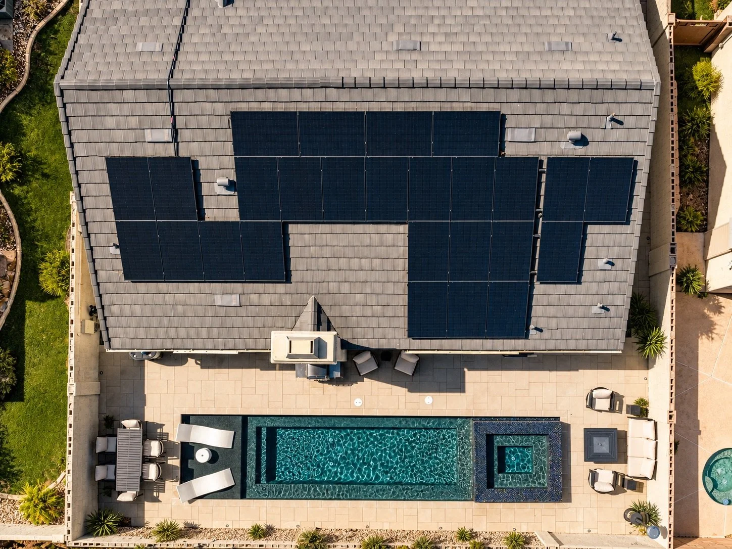 Aerial view of a house with solar panels on the roof, a backyard with a swimming pool, lounge chairs, and patio furniture, surrounded by greenery.