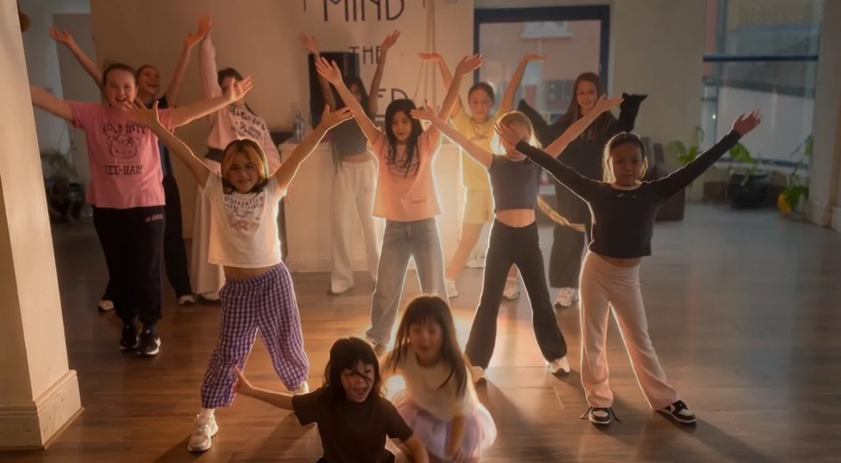 Children and teenagers dancing with arms raised in a room with wooden floors and large windows. Dublin kids dance class, Dublin teens activity, dublin teens dance class, dublin kids kpop dance class