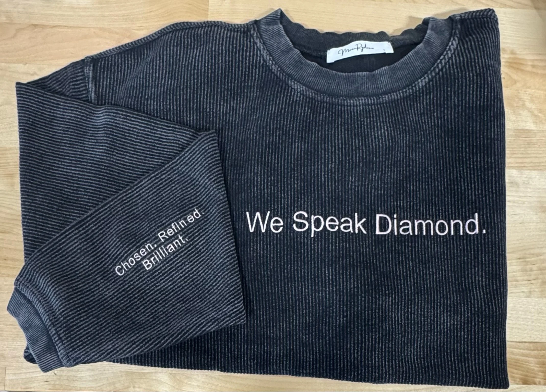 A folded dark gray striped T-shirt with white text that reads "We Speak Diamond" and other text partially visible underneath.