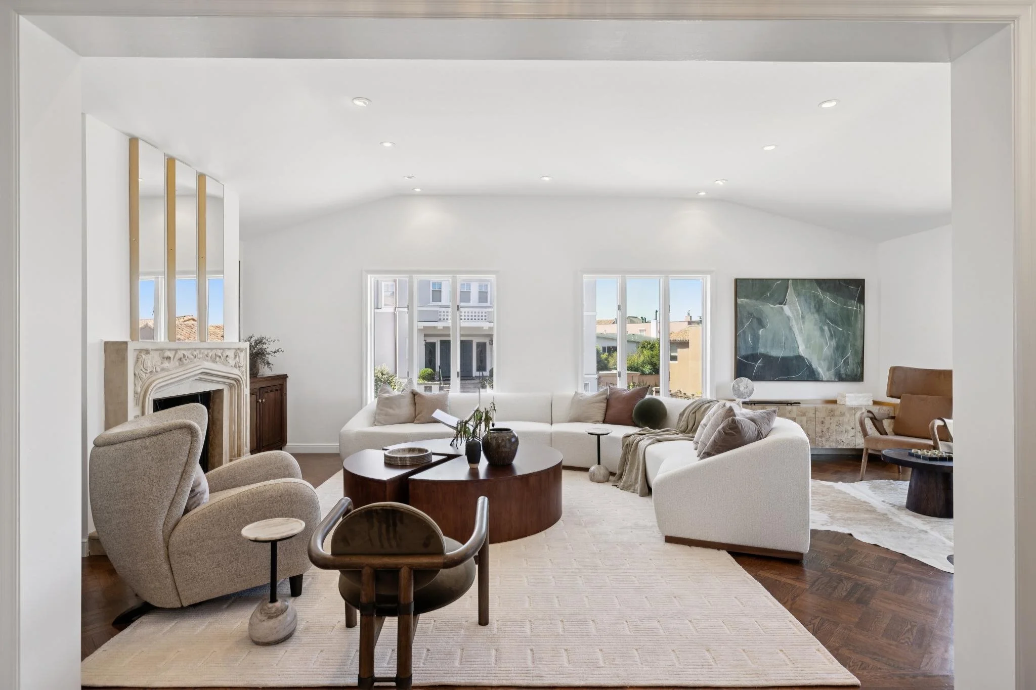 Living room with white walls, large windows, beige chairs, a white sectional sofa, and abstract wall art.