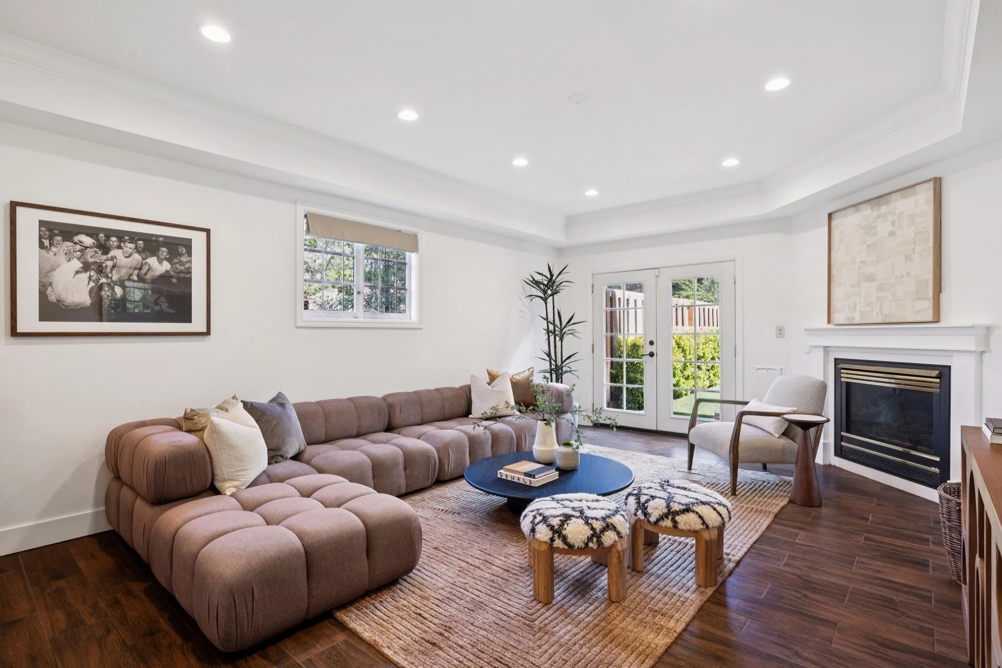Modern living room with a pink sectional sofa, white walls, a fireplace, artwork, and a large window with white framing and a door leading outside.