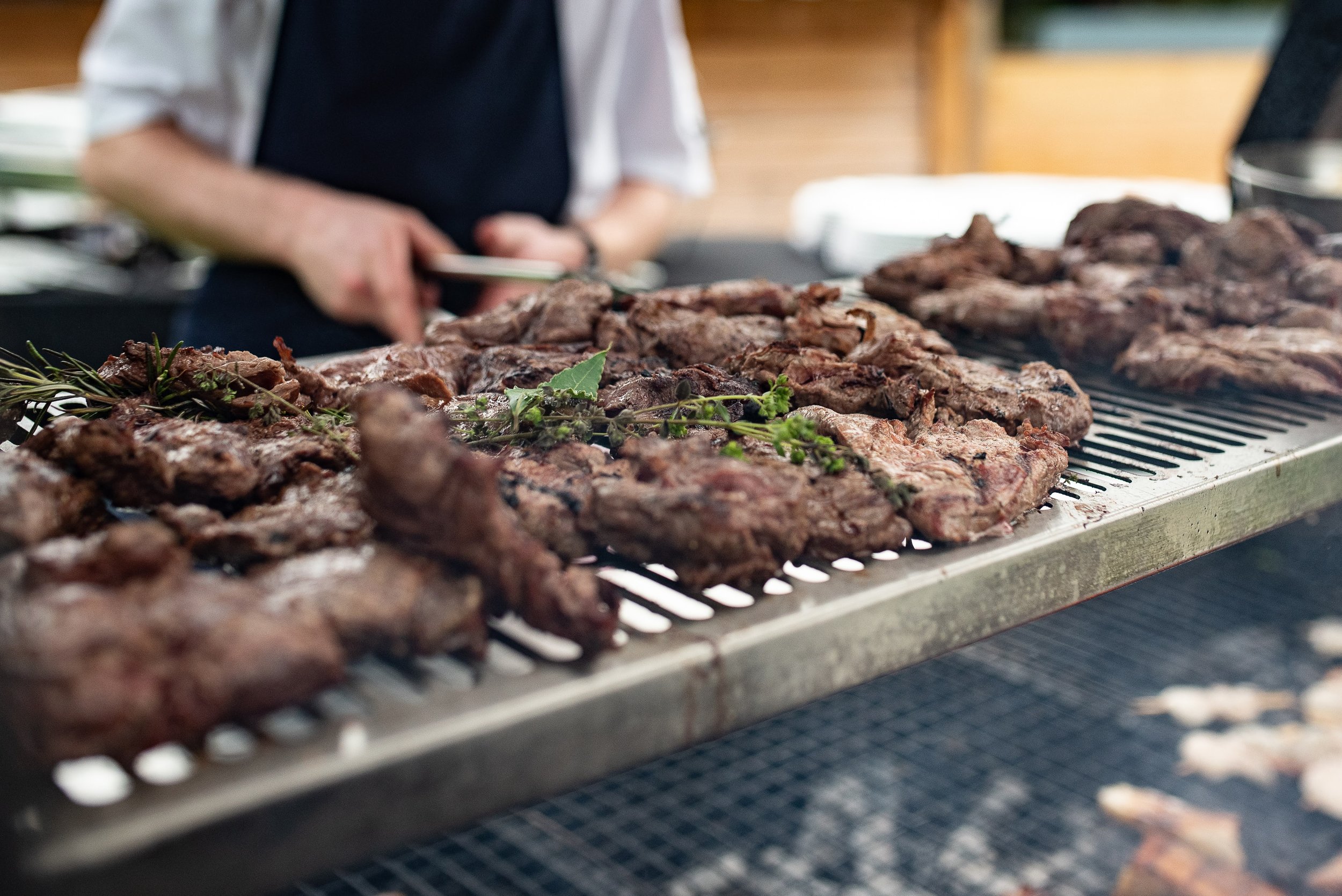 Various cuts of cooked meat on a grill with some herbs, likely during barbecue or grilling.