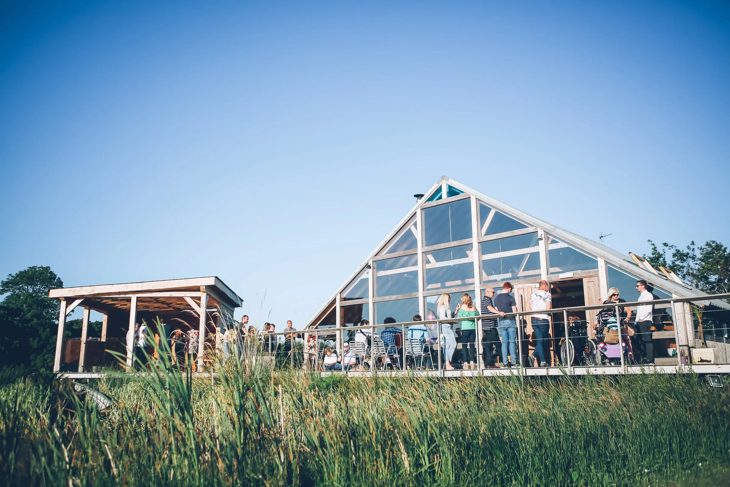 A group of people gathered outside a modern glass and wood building with a triangular roof, under a clear blue sky.