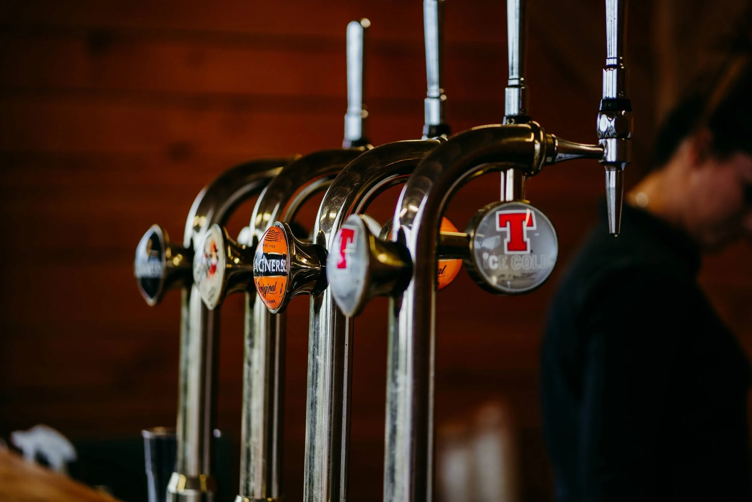 A row of beer taps with colorful labels attached, mounted on a metal bar against a dark background.