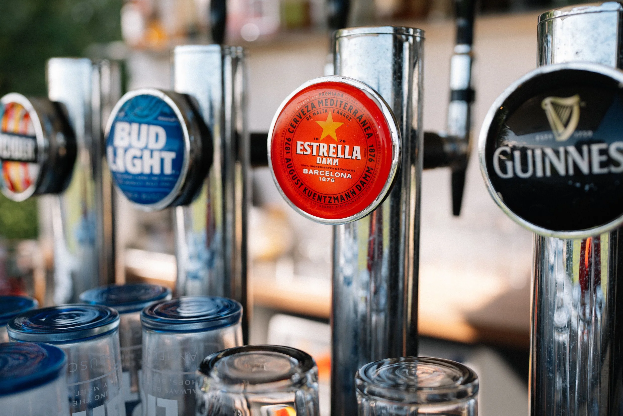 Close-up of a row of beer taps, with the middle tap labeled 'Estrella Damm', flanked by other taps with labels for Bud Light and Guinness.