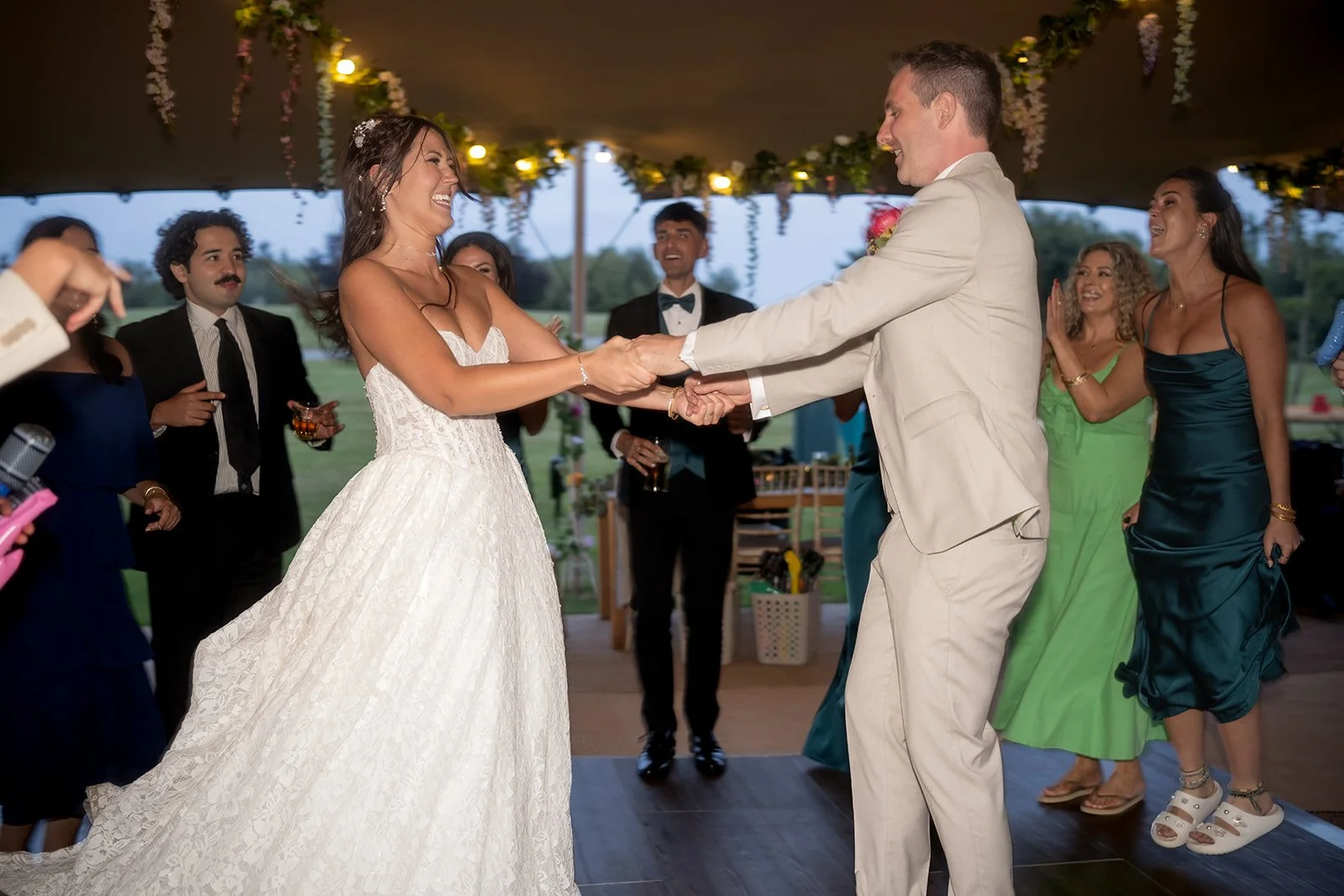 A bride and groom dancing at their wedding reception with friends smiling and watching around them.