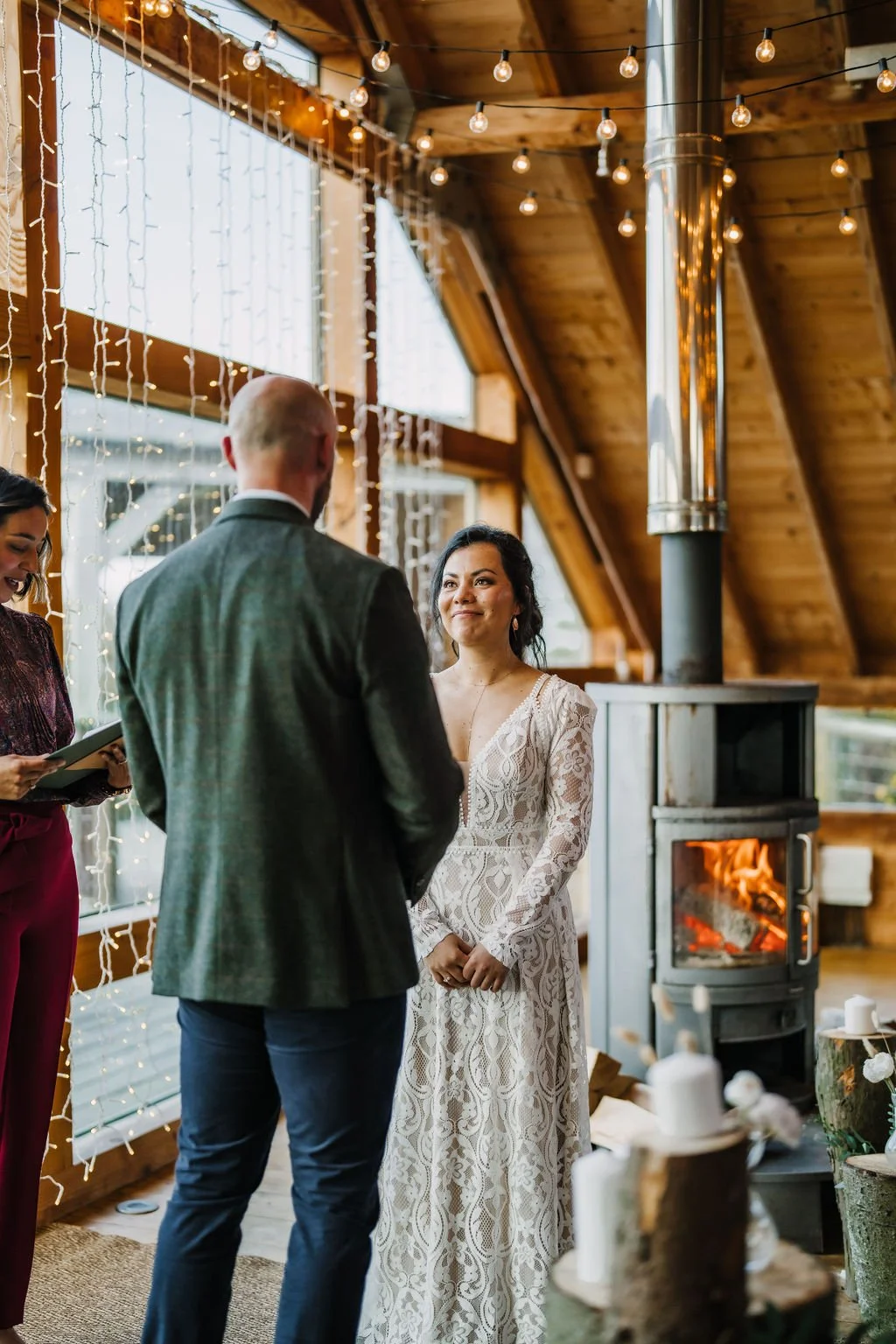 Woman in a wedding dress during a ceremony in a cozy, wood-paneled room with string lights and a fireplace.