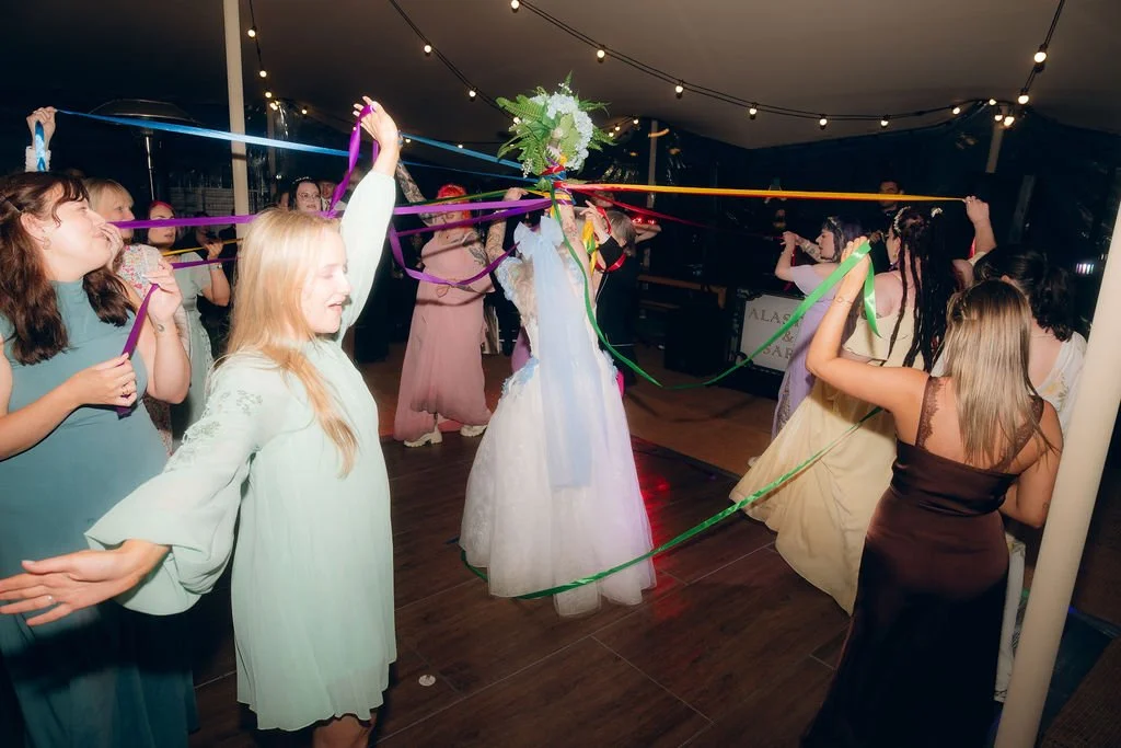 People participating in a ribbon dance at a celebration with string lights overhead.