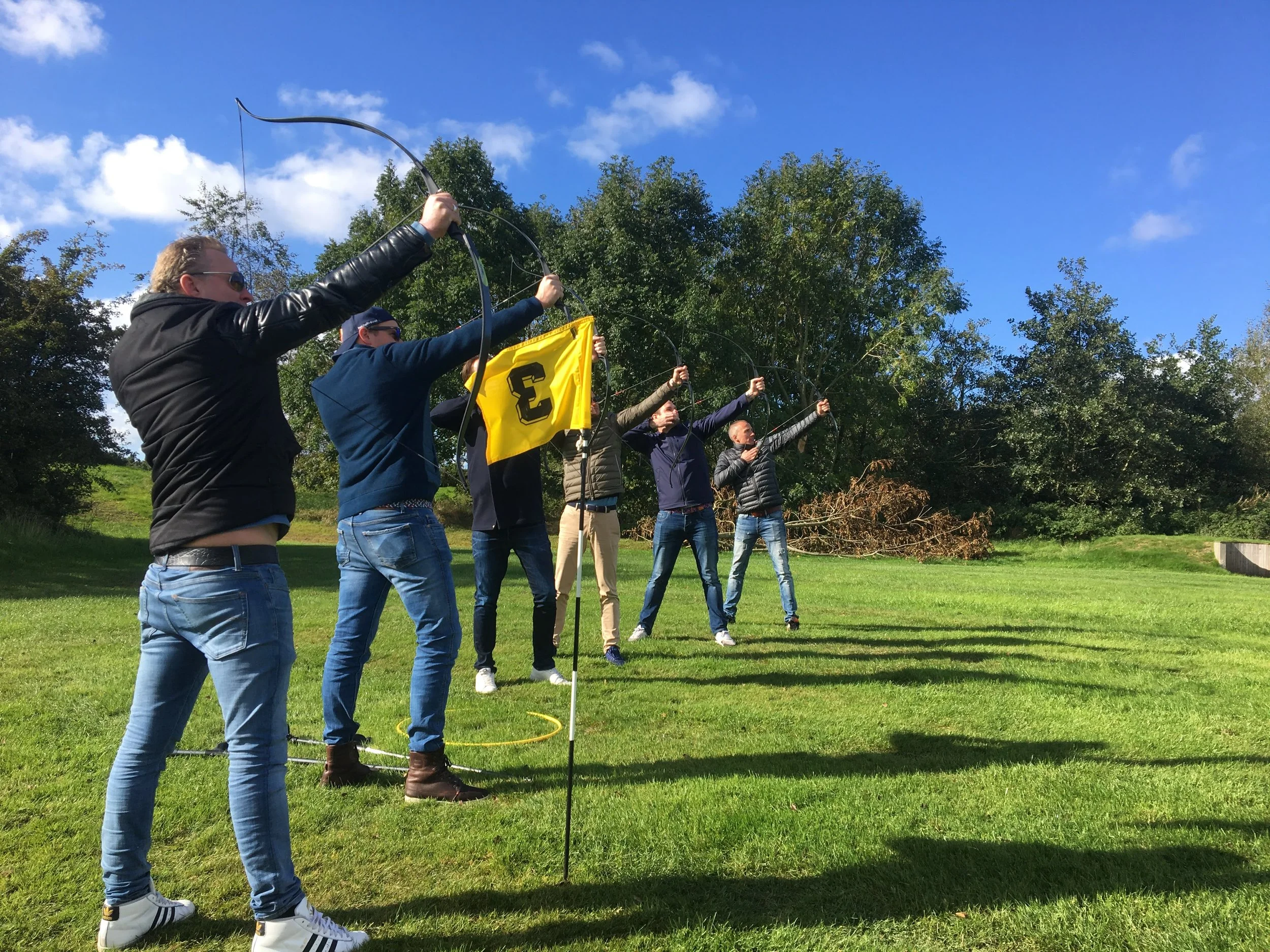 Group of people standing outdoors in a park on a sunny day, releasing doves with a yellow dove release flag, surrounded by green trees and blue sky.