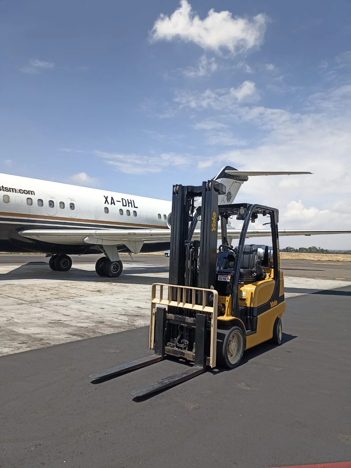 Una grúa elevadora amarilla en un aeropuerto y un avión grande en el fondo, en un día soleado y despejado.