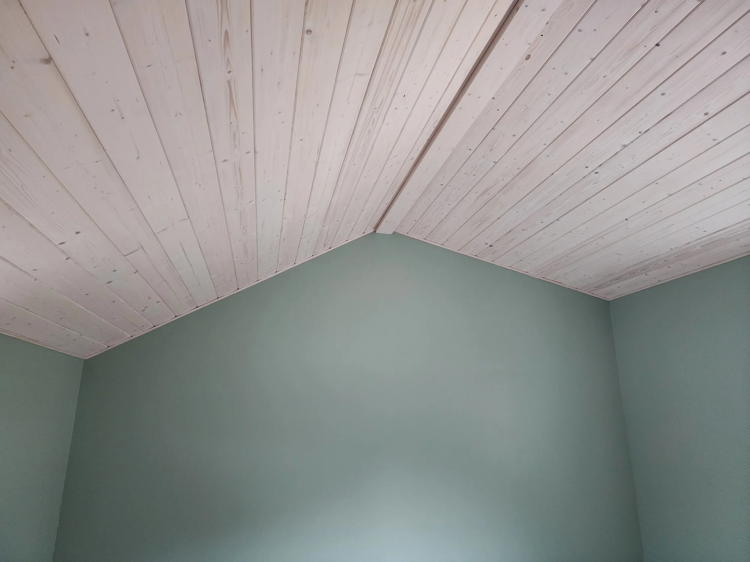 A ceiling with light-colored wooden panels and a green wall below.