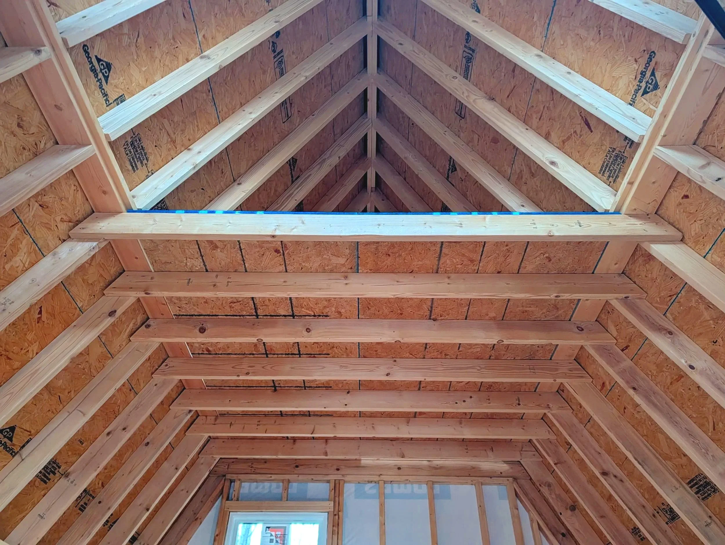 The interior view of a wooden roof framing with exposed beams and plywood sheathing, showing the construction of a building's roof.