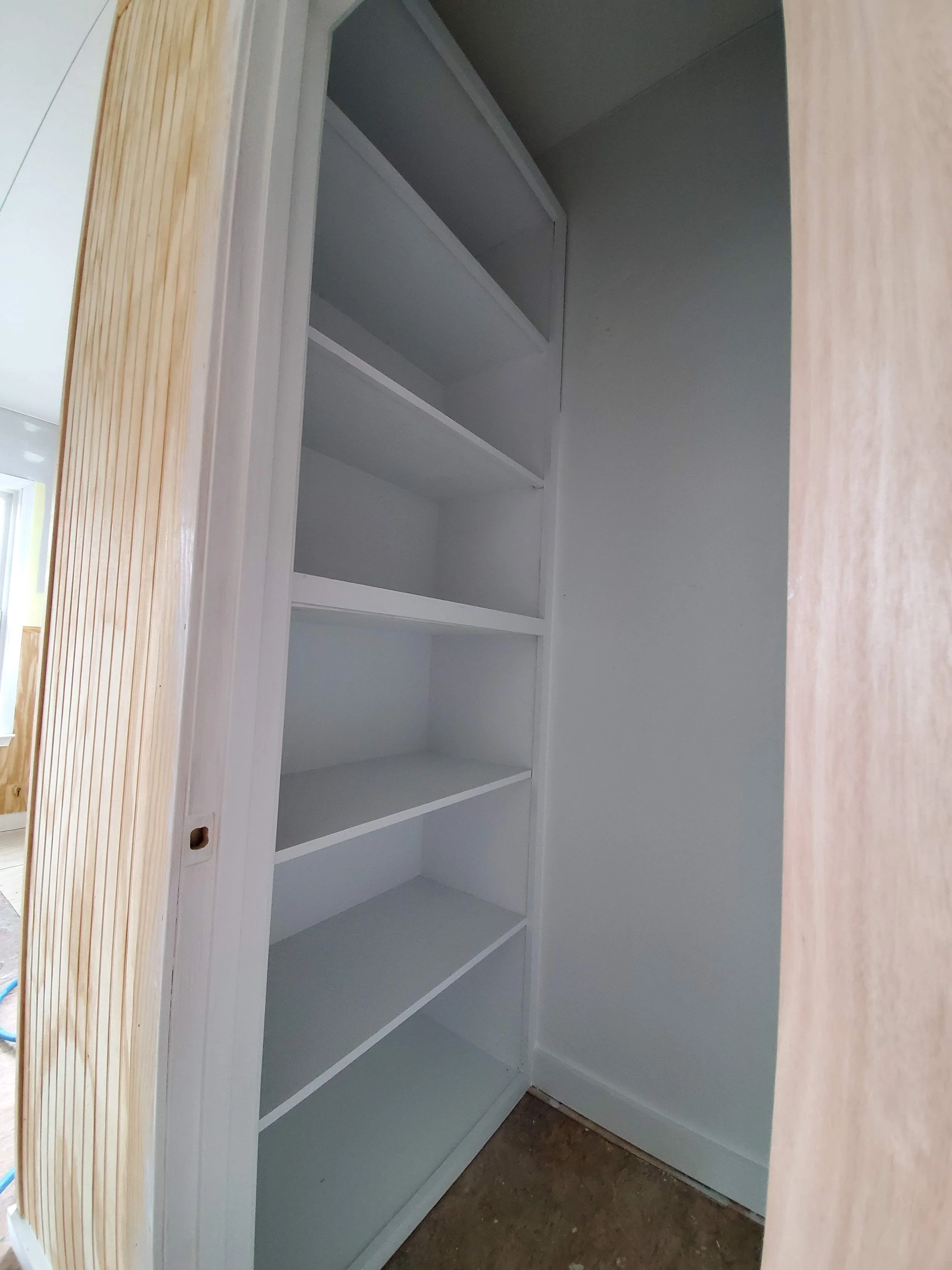 Empty white shelving unit inside a closet or pantry, framed by a wooden doorframe.