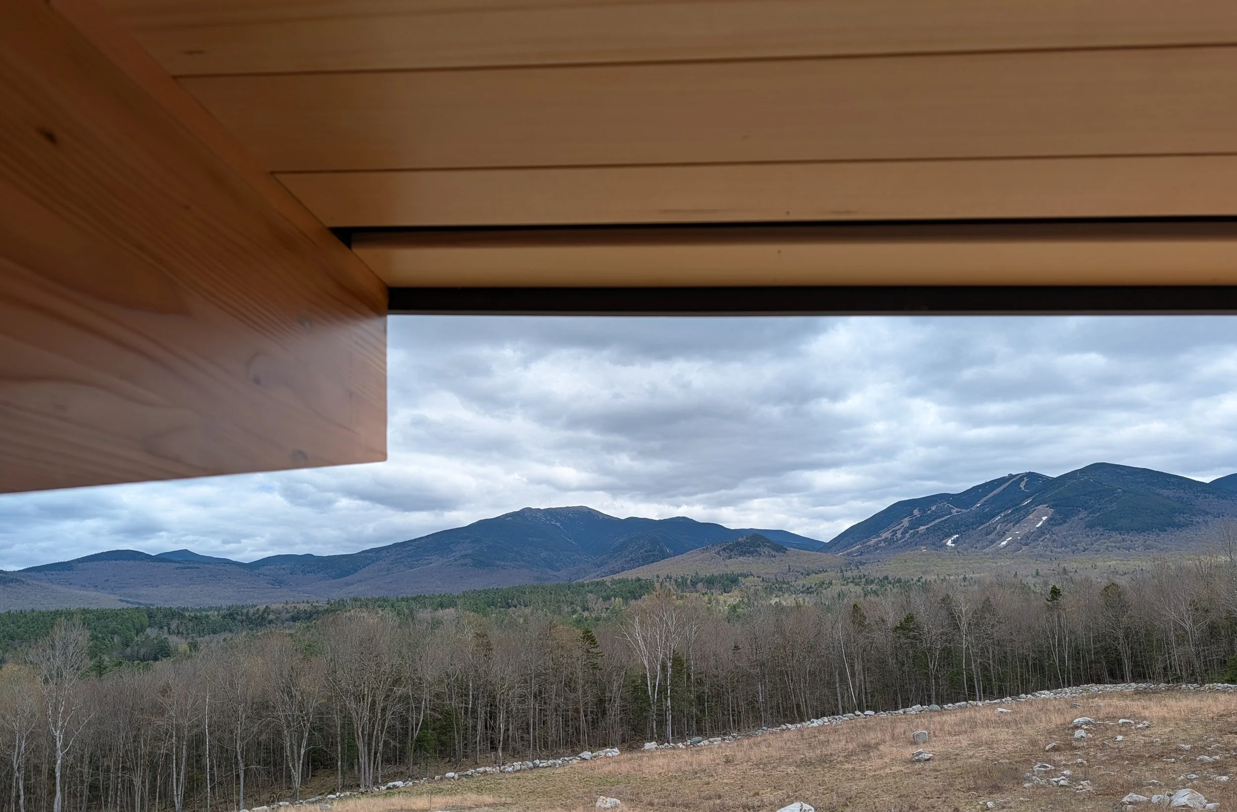 View of mountains with a cloudy sky from under a wooden overhang.