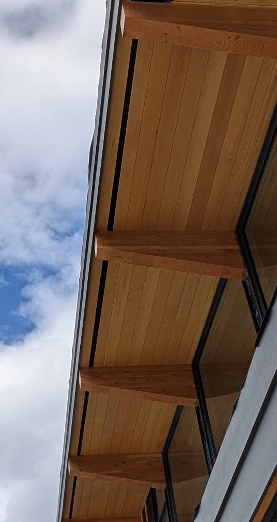 Close-up view of a wooden exterior wall of a building with sky and clouds in the background.