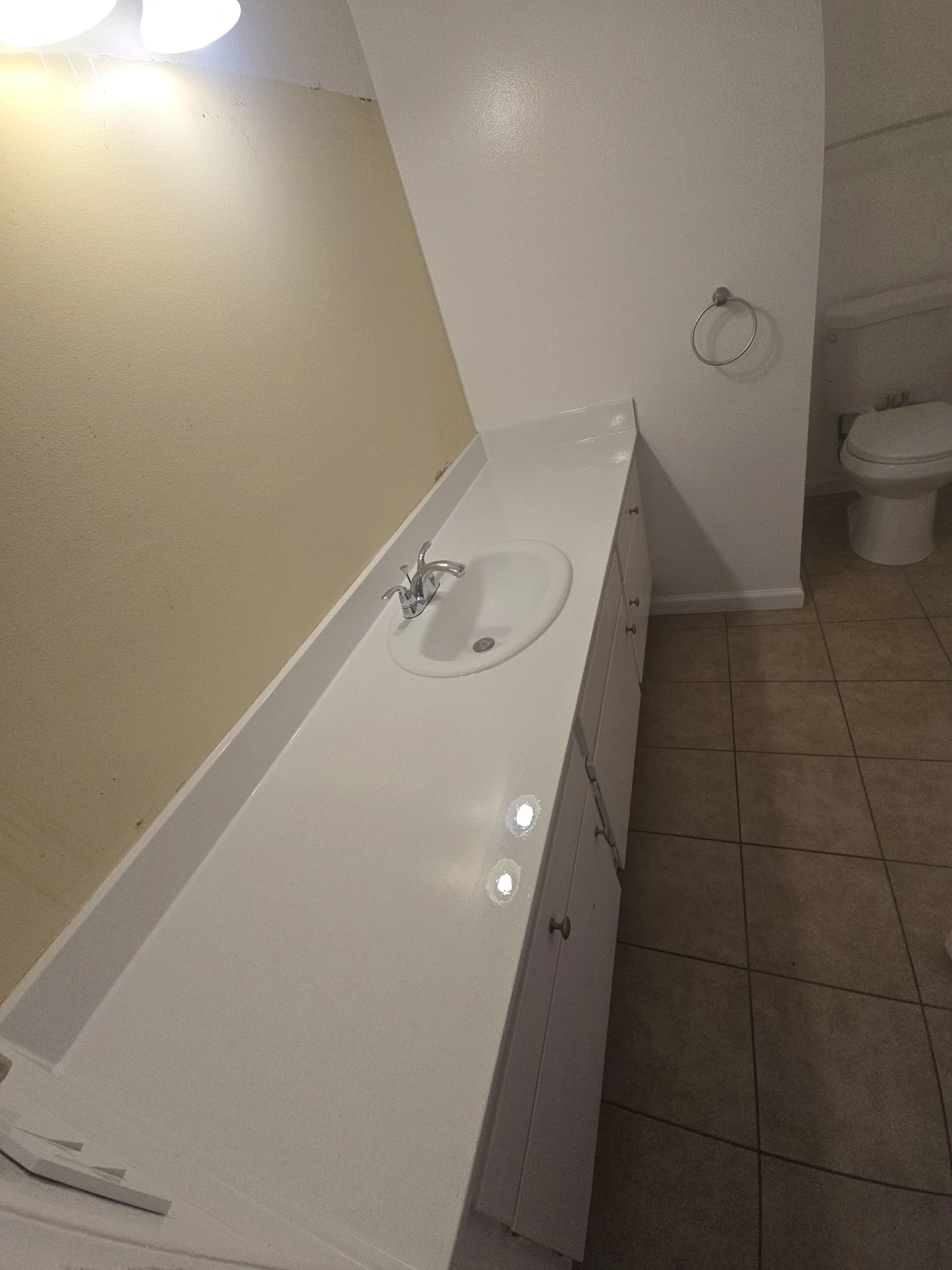 Bathroom with a white vanity, sink, faucet, beige wall, and part of a toilet visible.