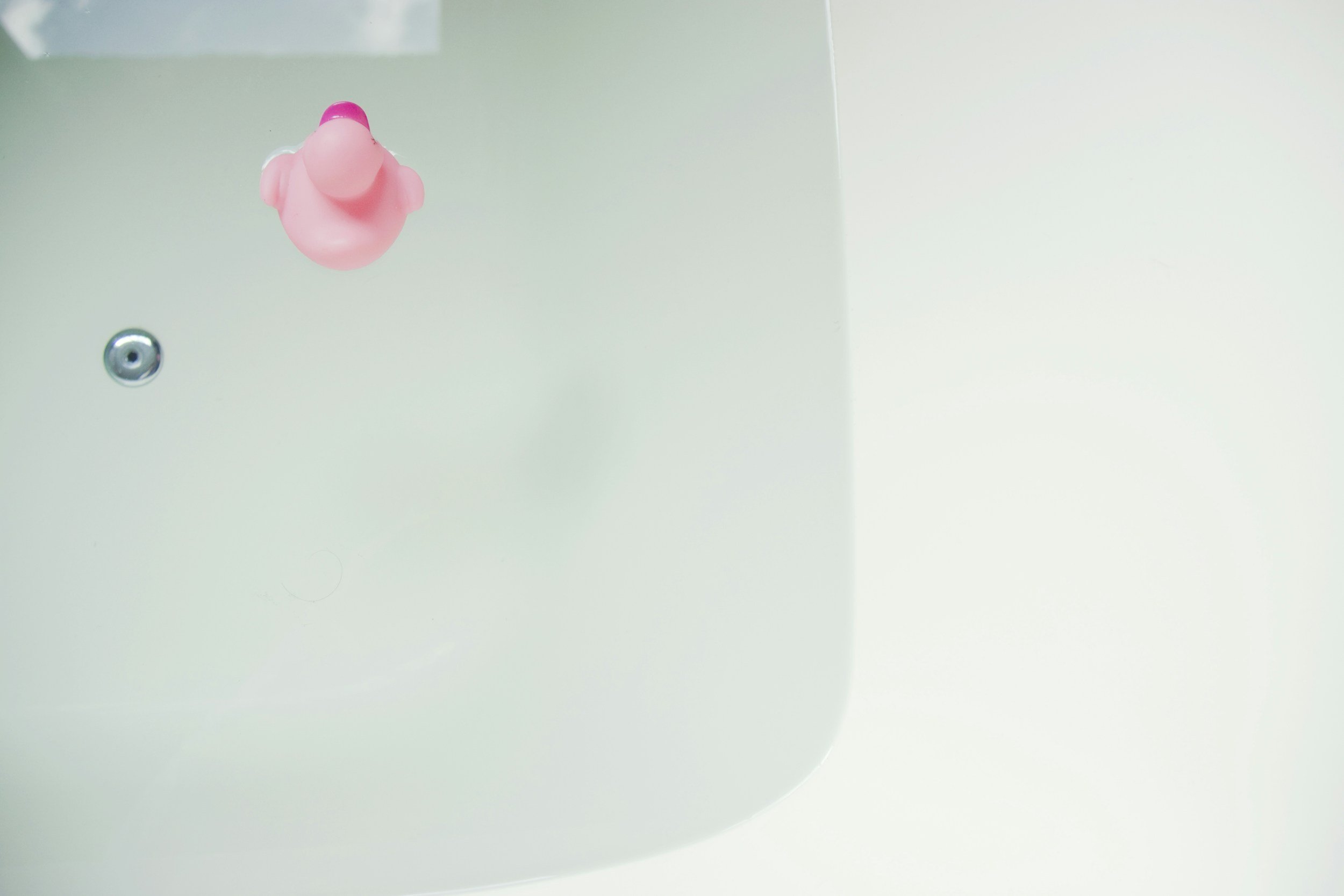Close-up of a white porcelain toilet with a pink rubber duck on top of the tank.