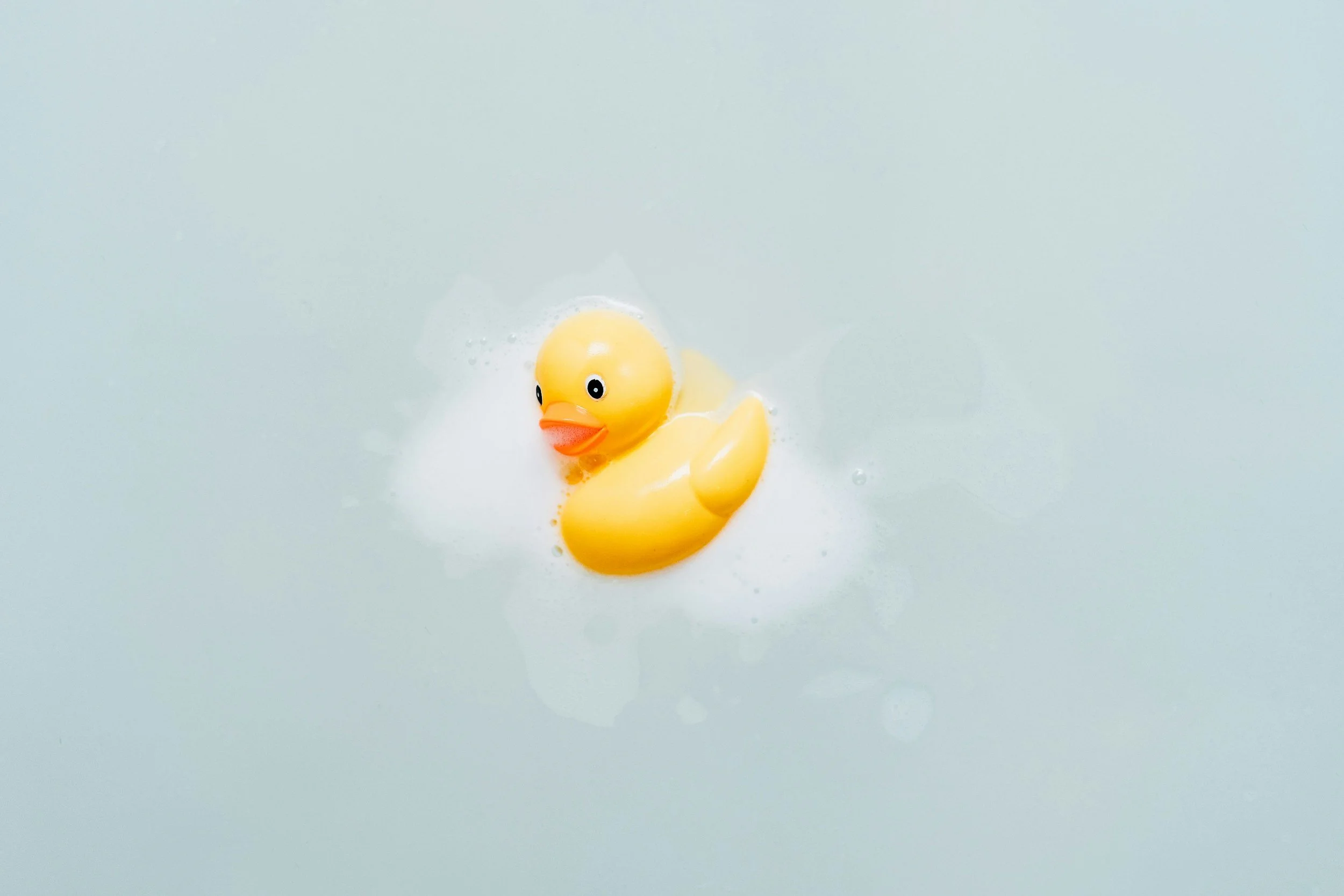 A yellow rubber duck floating on water in a bathtub.