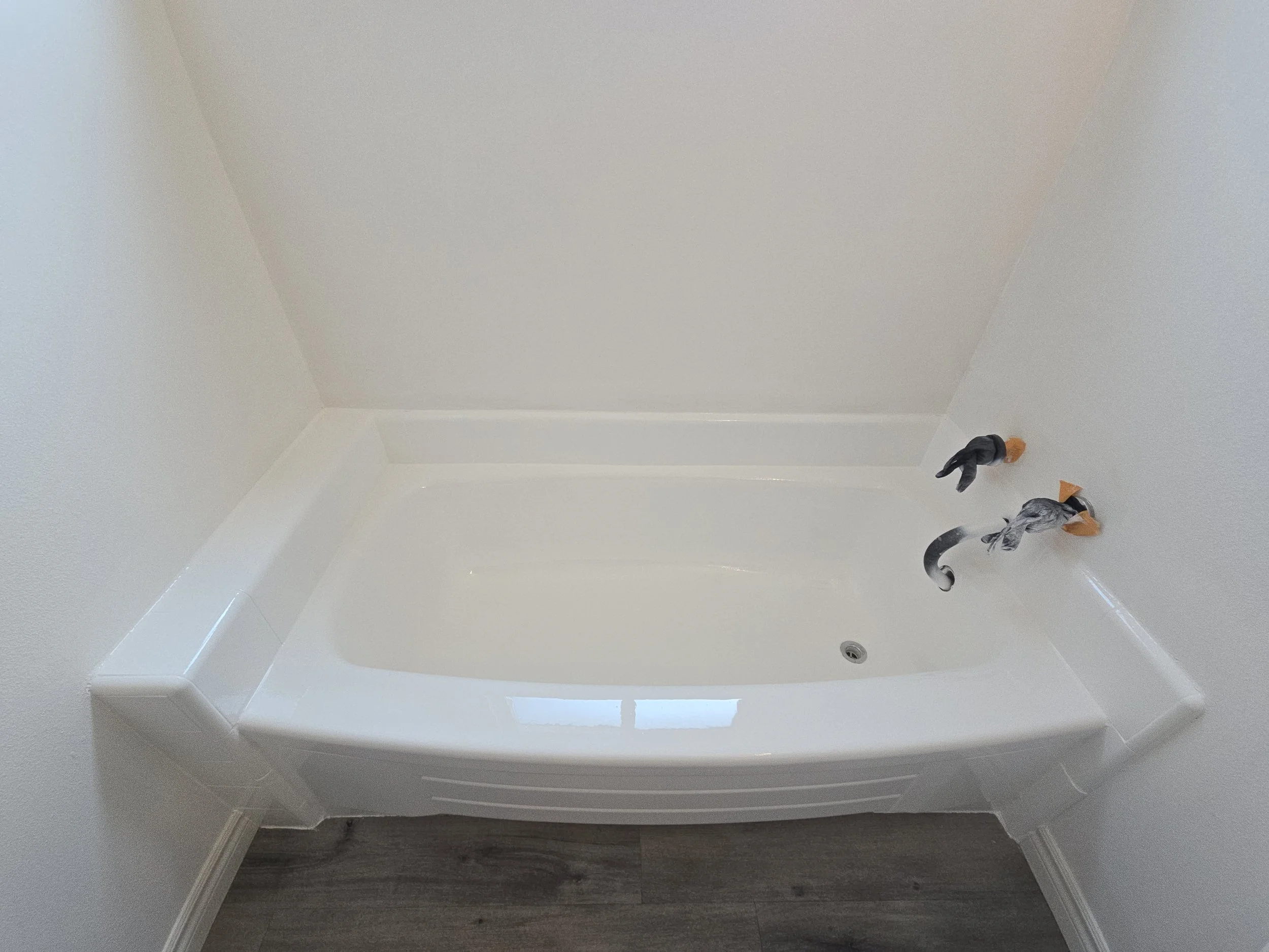 Bathroom with a white bathtub, wall-mounted water fixtures, and some construction tools and materials nearby.