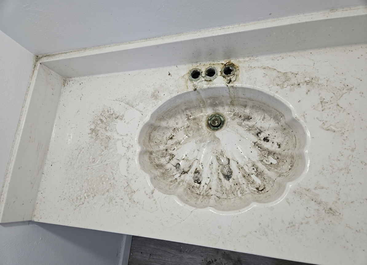 Dirty bathroom sink with grime, soap scum, and mold around the drain and back surface.