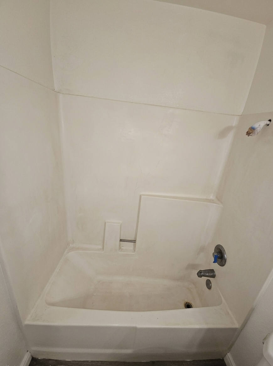 Empty bathtub shower area with old fixtures and a small built-in ledge
