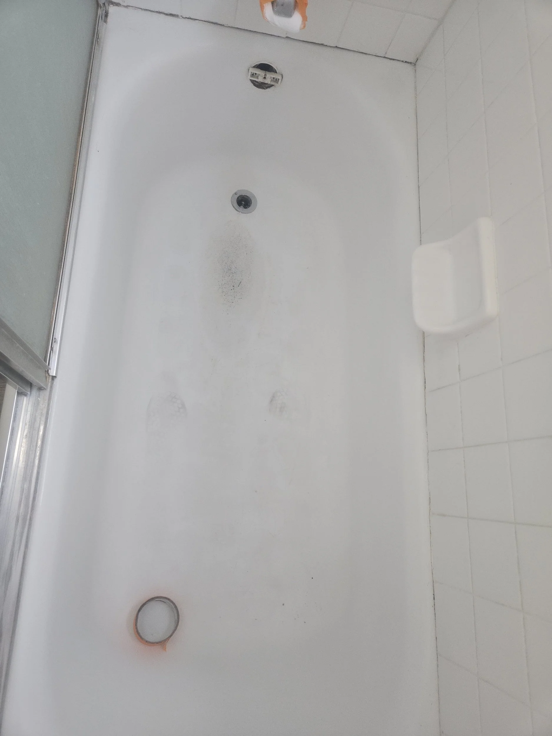 Empty shower with a white wall, a drain in the floor, and a shower head. The shower head is covered with orange painter's tape.