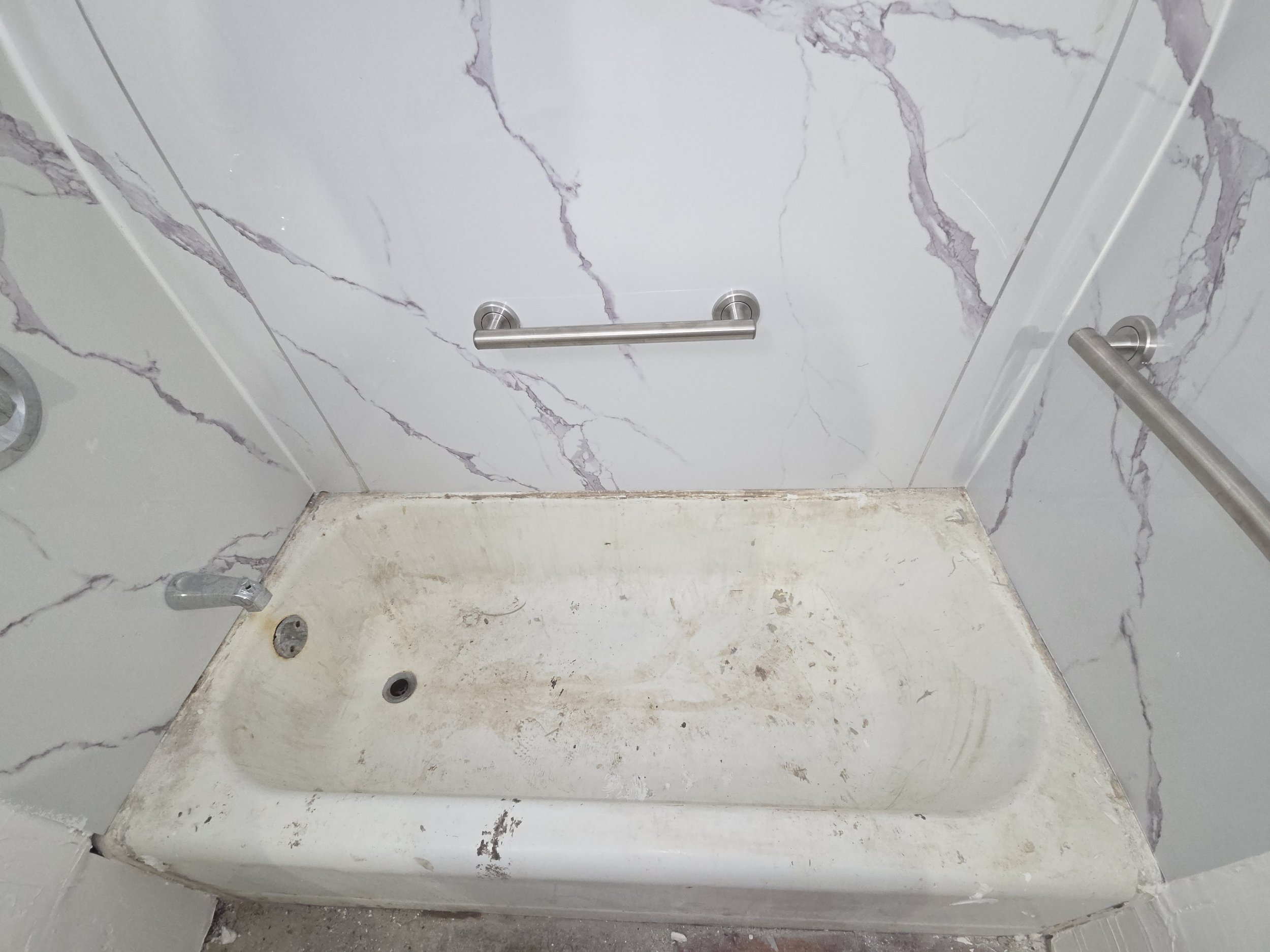 Marble shower wall with metal handle, dirty white tub, and visible mold and dirt at the base.