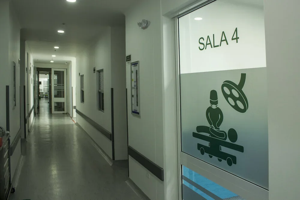 Pasillo en un hospital con puertas a los lados y señalización que indica la Sala 4, con icono de un cirujano y equipo médico.
