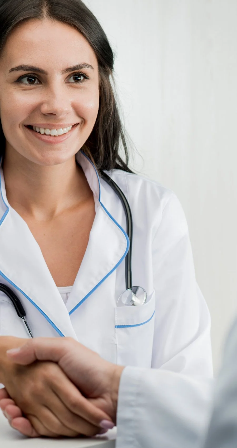 Médica sonriendo y dando la mano a un paciente, vistiendo bata blanca y con estetoscopio alrededor del cuello.