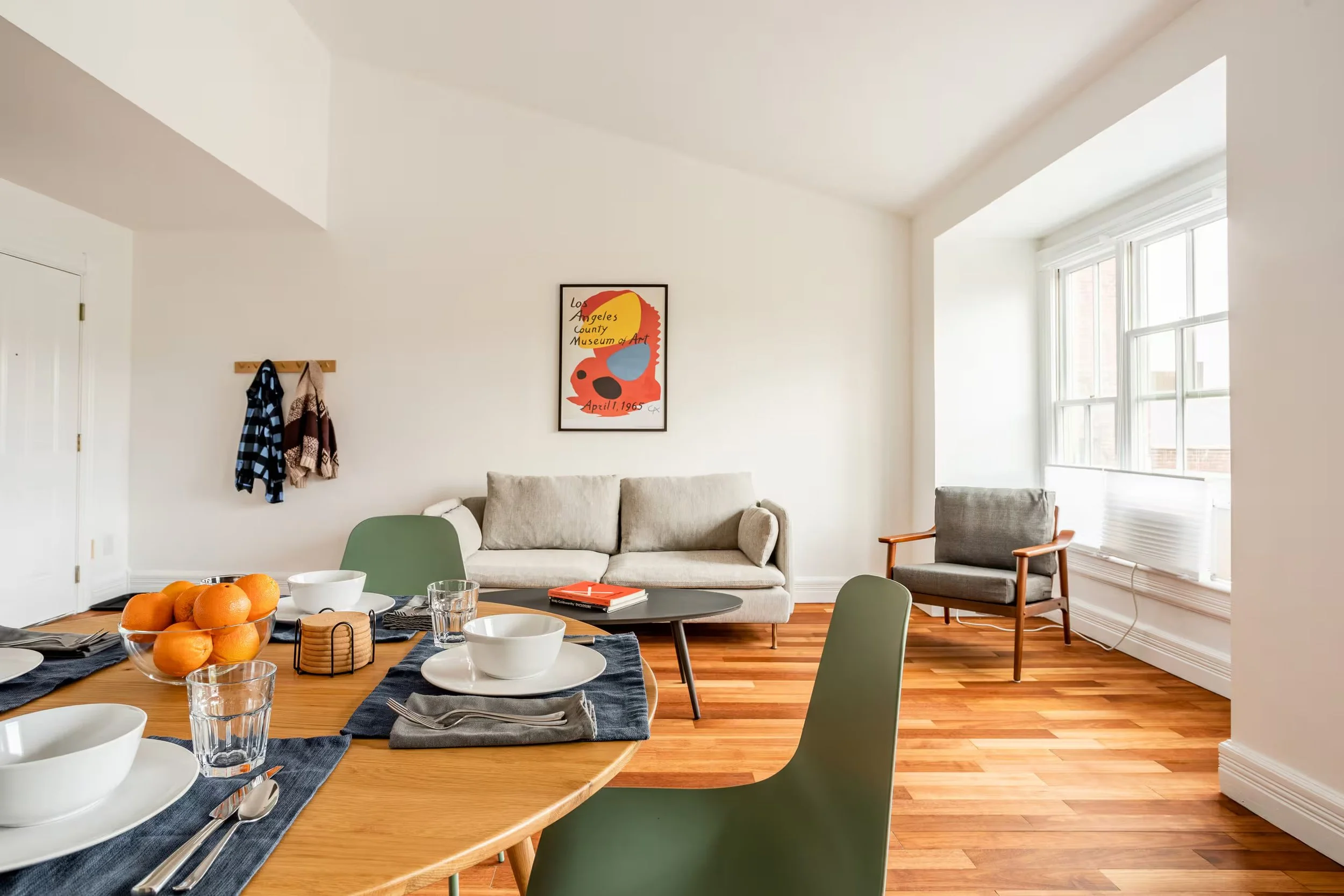 Bright living and dining area in a Catskill Village vacation apartment, featuring hardwood floors, a dining table set for four, and comfortable seating.