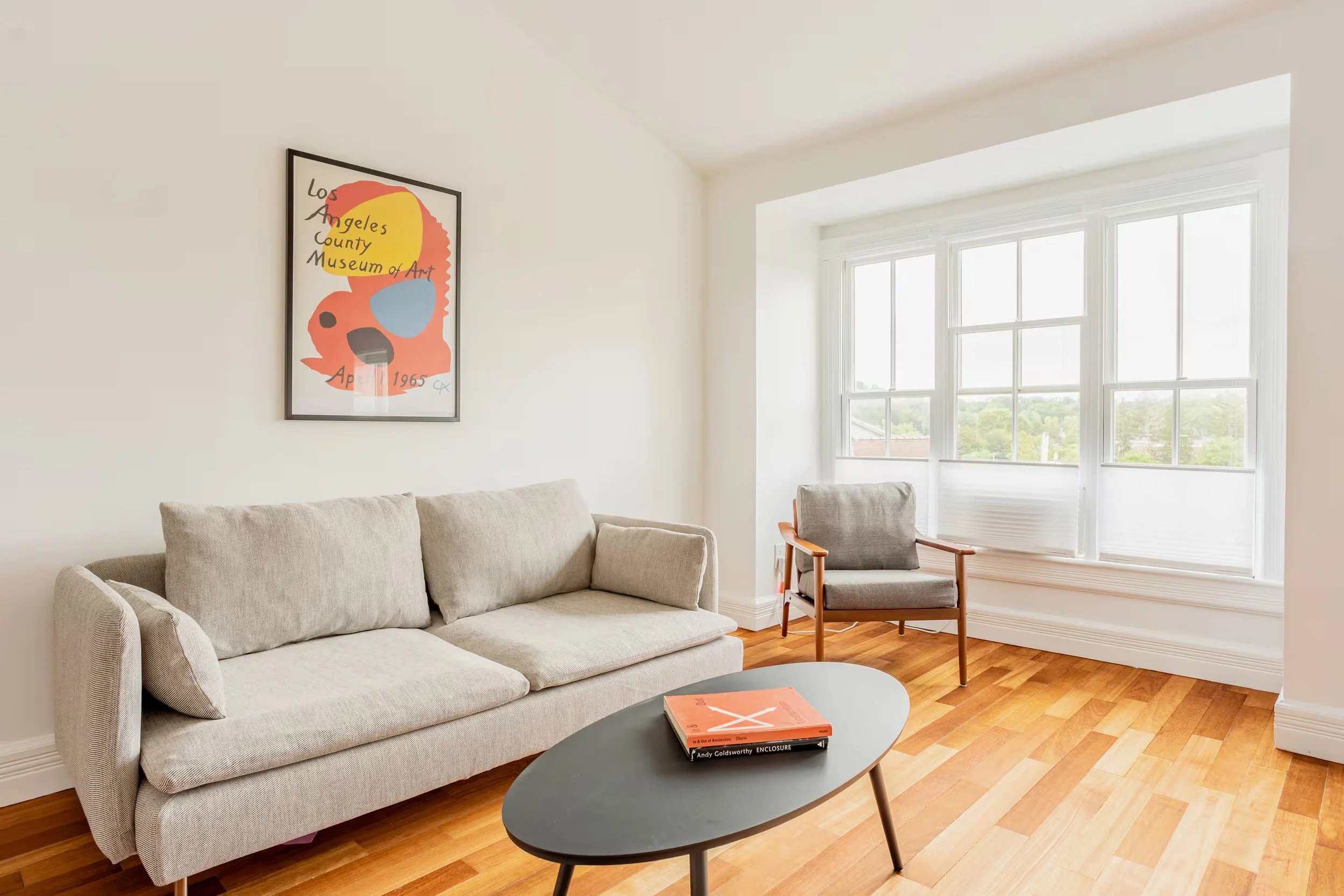Sunlit living room at Above SpringRise vacation apartment in Catskill, NY, featuring a comfortable sofa, armchair, hardwood floors, and large windows.