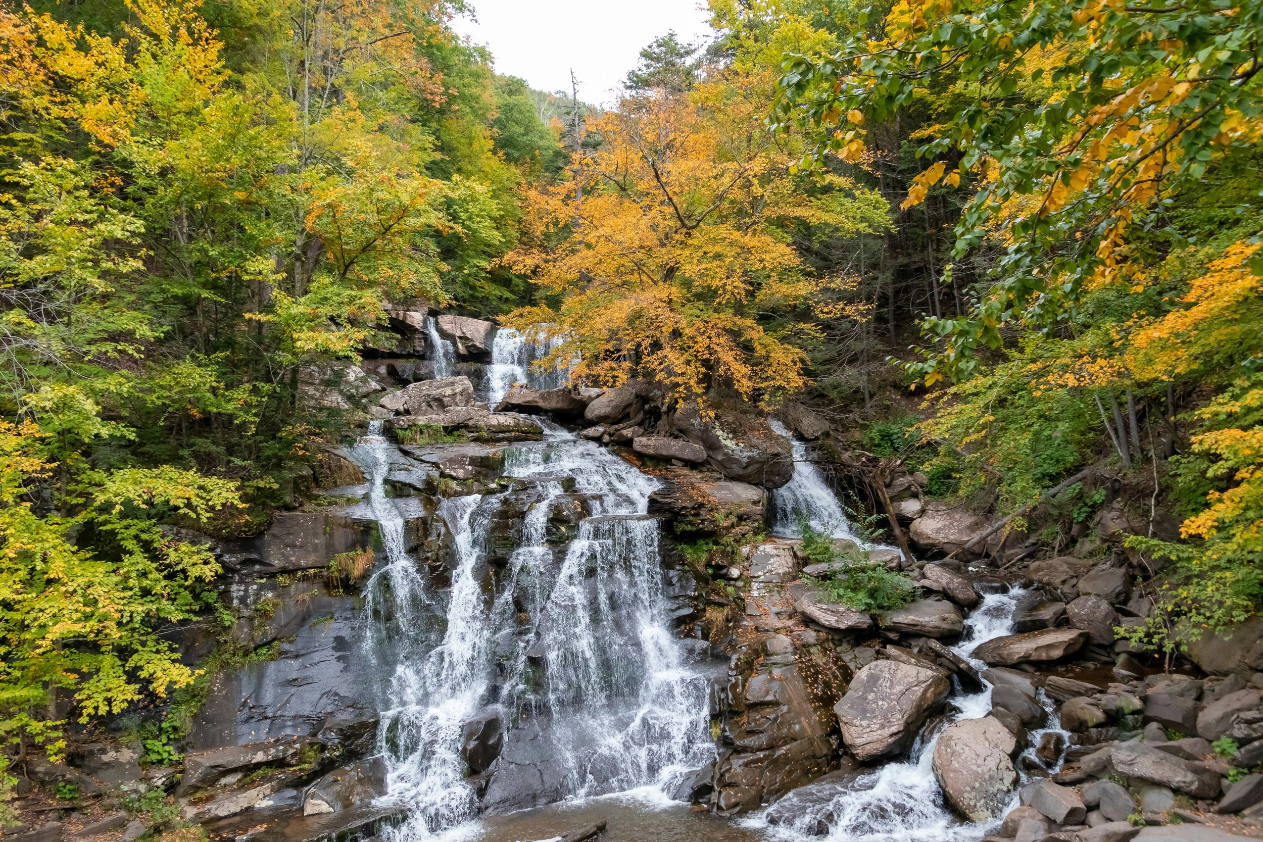 Waterfall cascading over rocky ledges surrounded by colorful autumn foliage in the Catskill Mountains of New York.